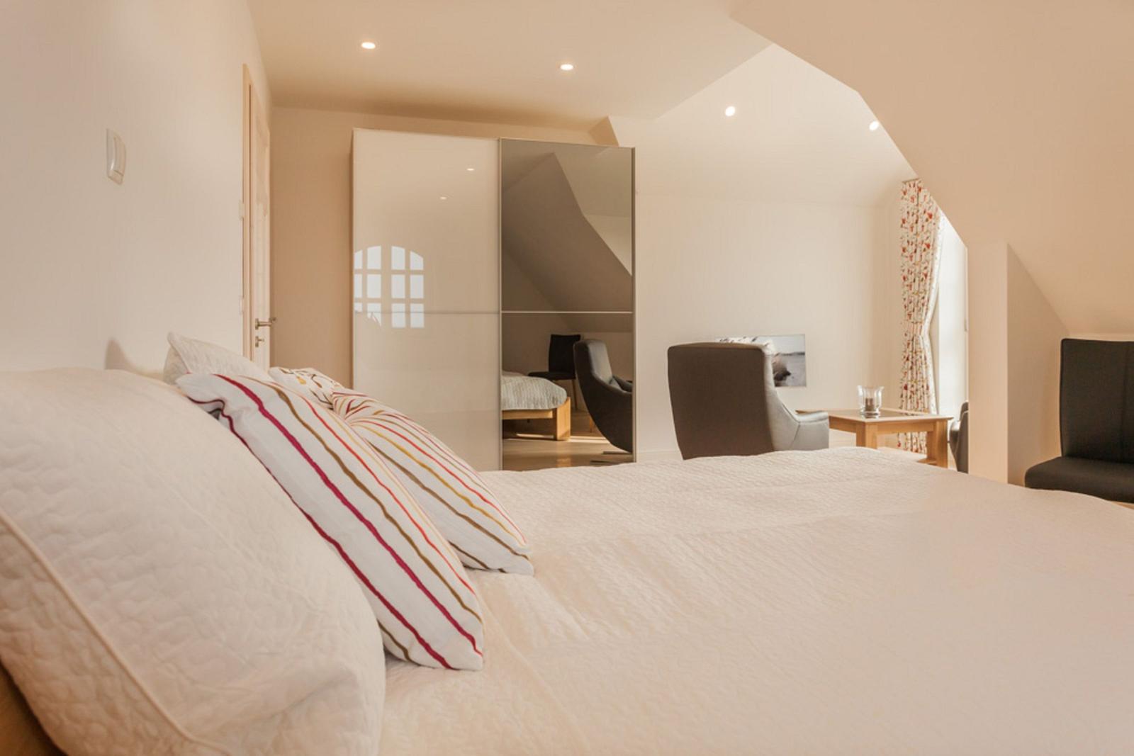 Schlafzimmer mit Bett, Spiegelschrank und Sitzgelegenheiten unter Dachschrägen.