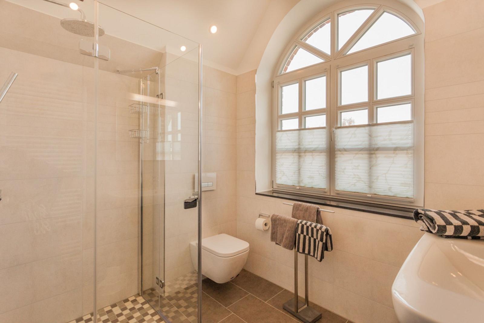 Badezimmer mit Dusche, Toilette und Fenster.