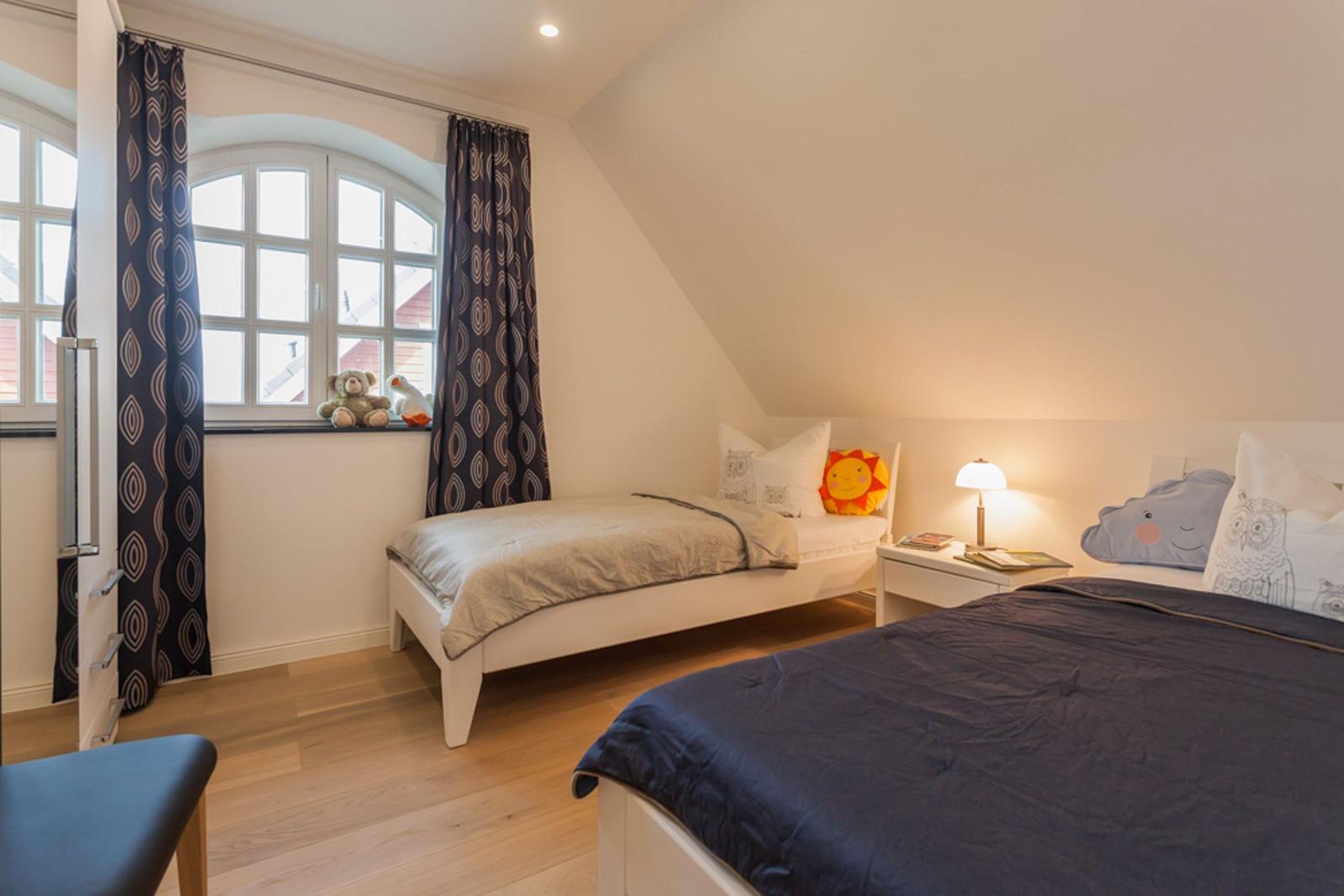 Zwei Betten mit Kissen und Decken, Fenster mit Vorhängen und Nachttisch mit Lampe.