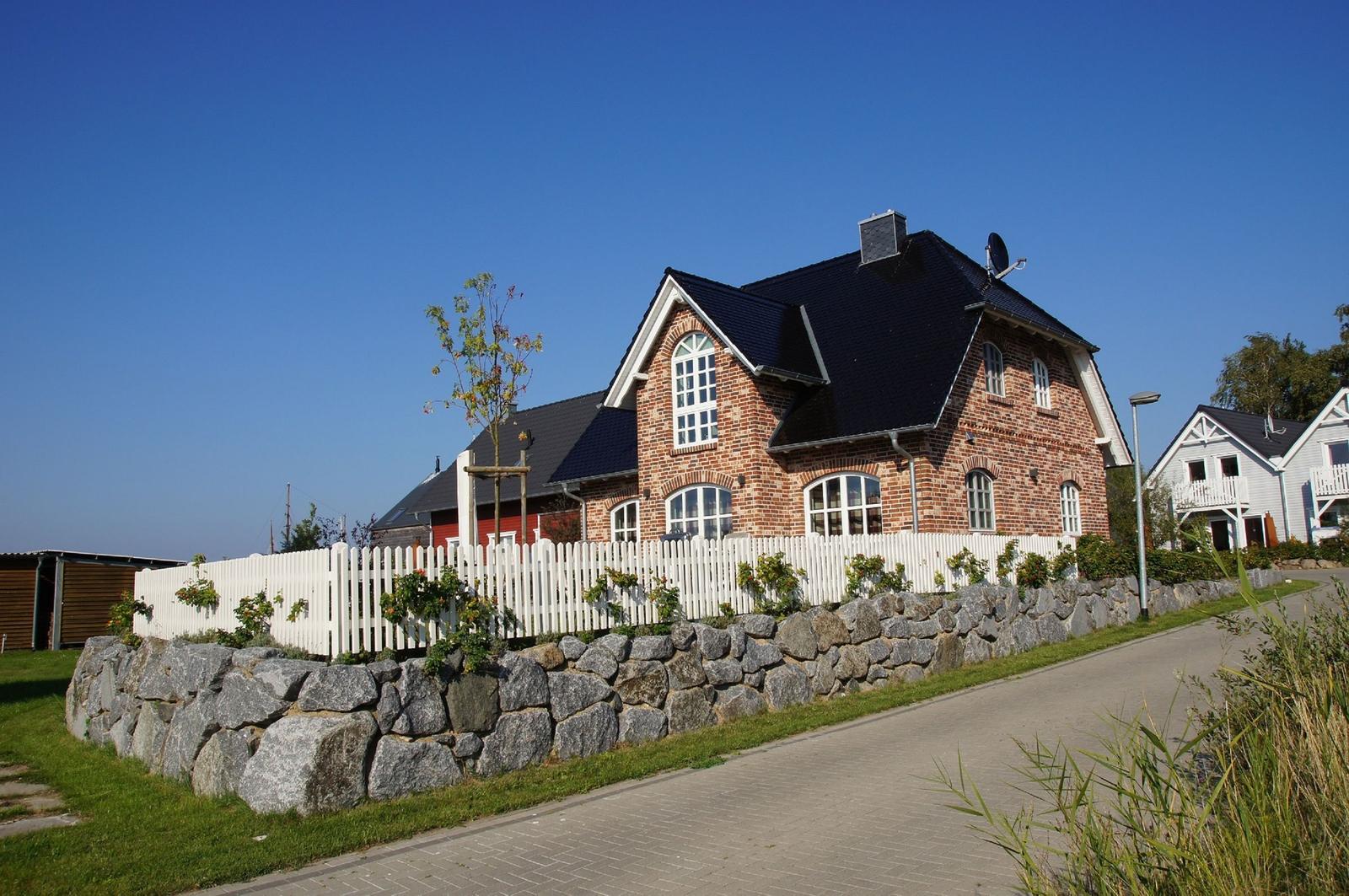 Haus mit rotem Ziegelstein, weißem Zaun und Steinmauer an Straße
