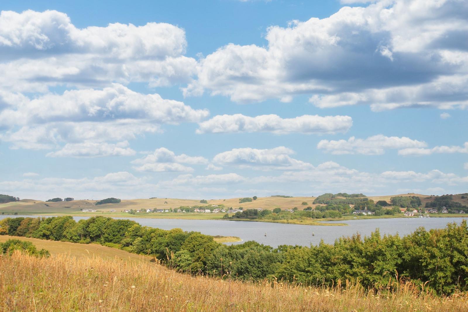 Weitläufiger See mit grünen Uferzonen und bewölktem Himmel.