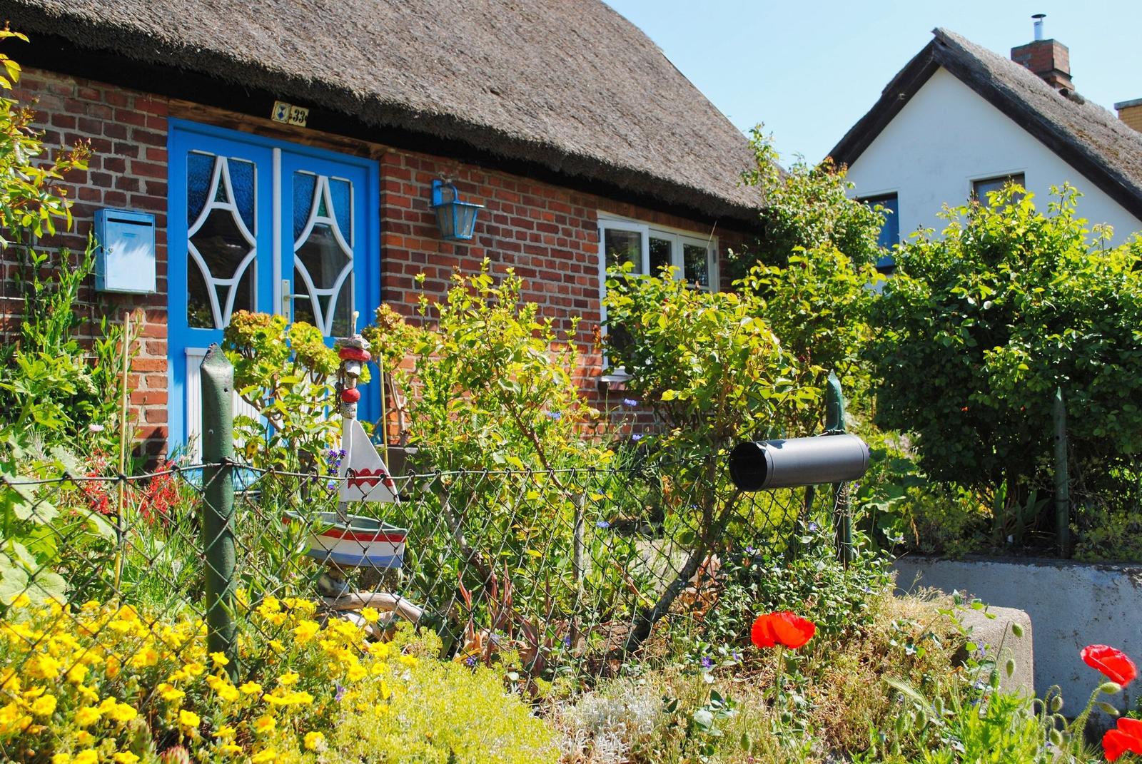 Haus mit strohgedecktem Dach, blauer Tür und grünem Garten mit Blumen.