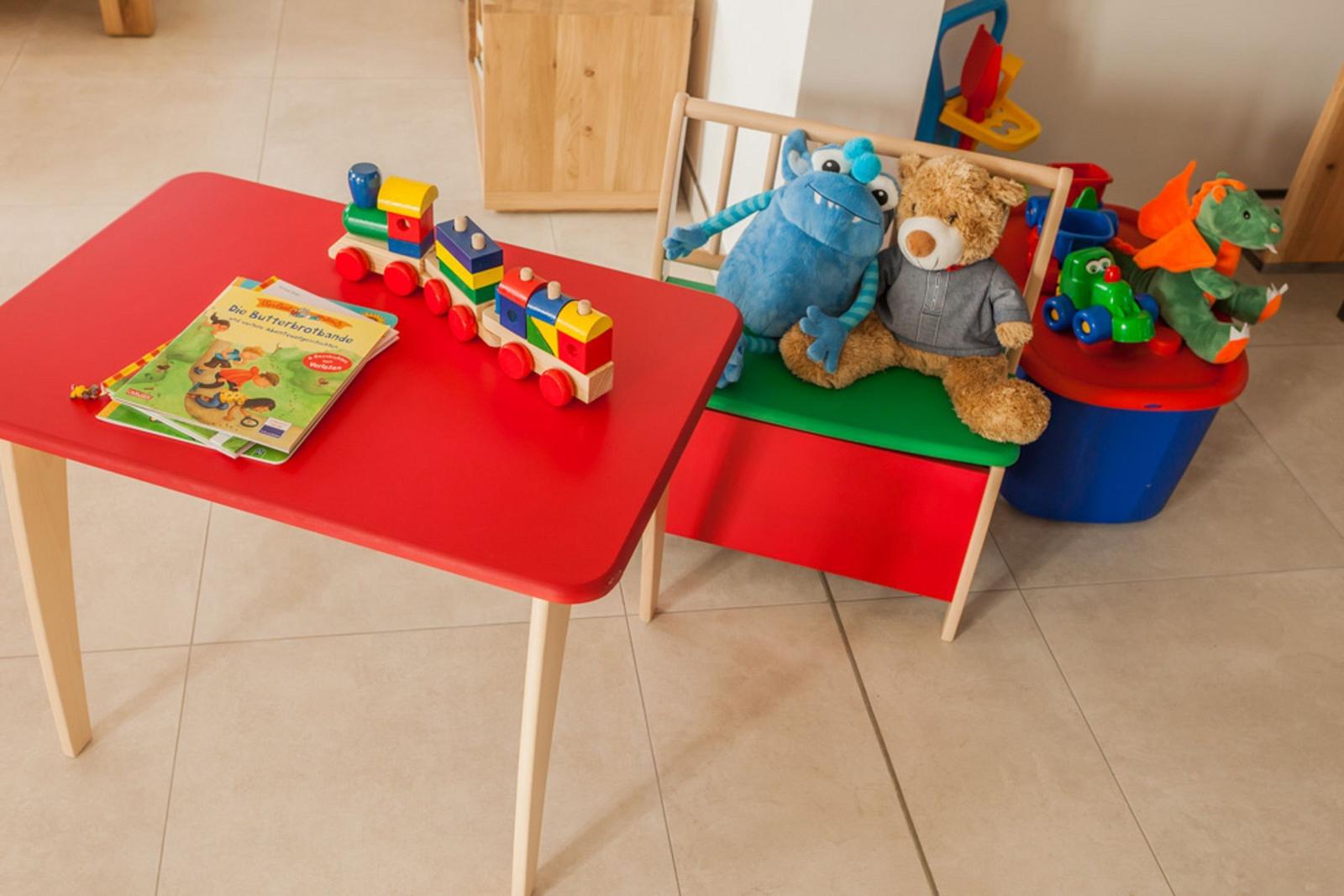 Roter Kindertisch mit Buch und Zug. Hocker mit Plüschtieren und Spielzeugkasten.