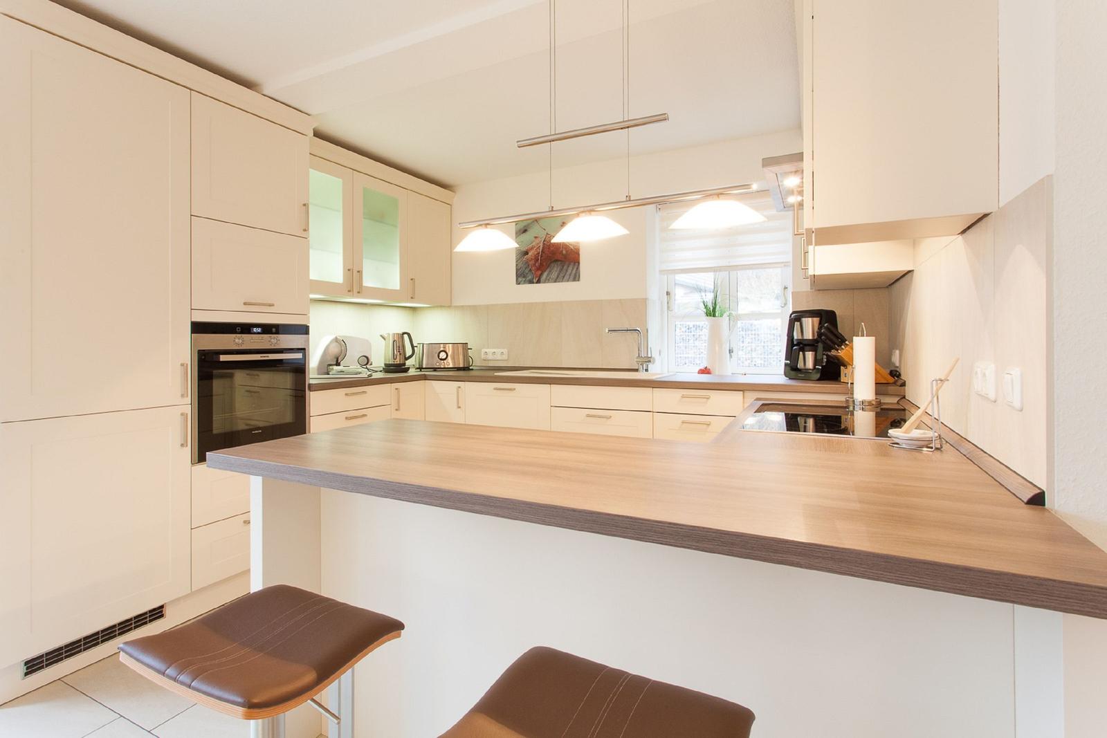 Moderne Küche mit Holzoberfläche und integriertem Herd. Barhocker und Fenster sichtbar.