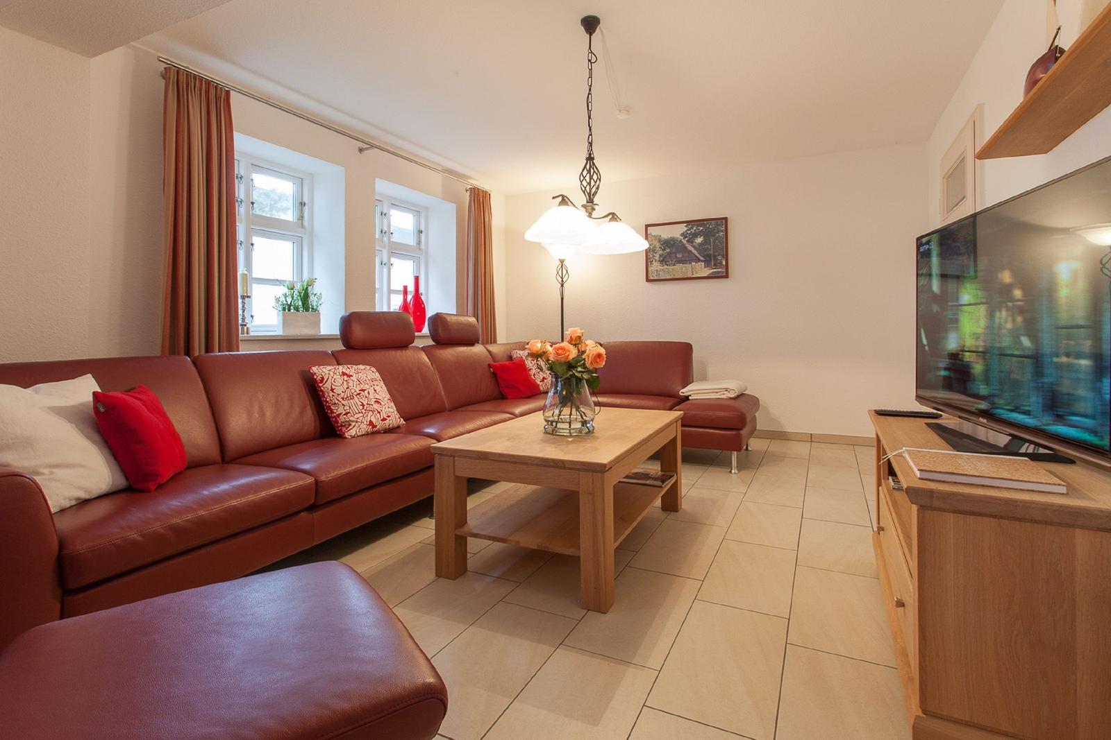 Ein Wohnzimmer mit rotem Ledersofa, Holztisch und Fernseher.