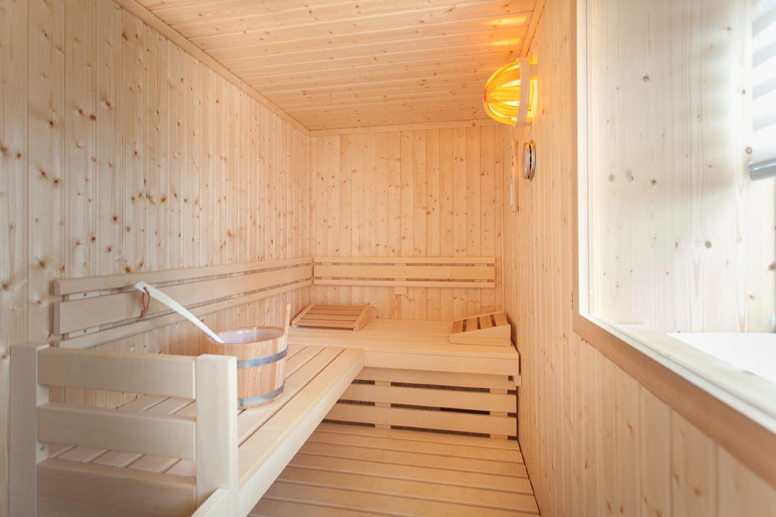 Holzsauna mit Sitzbänken, Eimer und warmem Licht an der Wand.