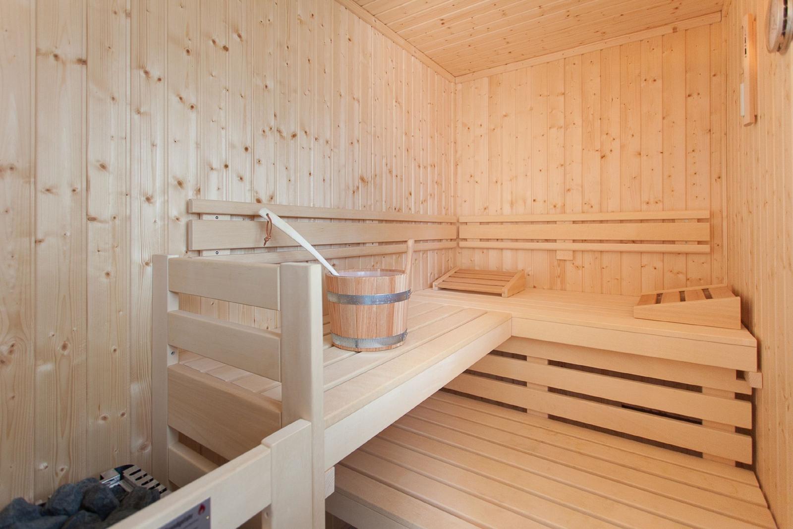 Sauna mit Holzbank und Eimer. Holzwände und -boden. Drei Sitzstufen.