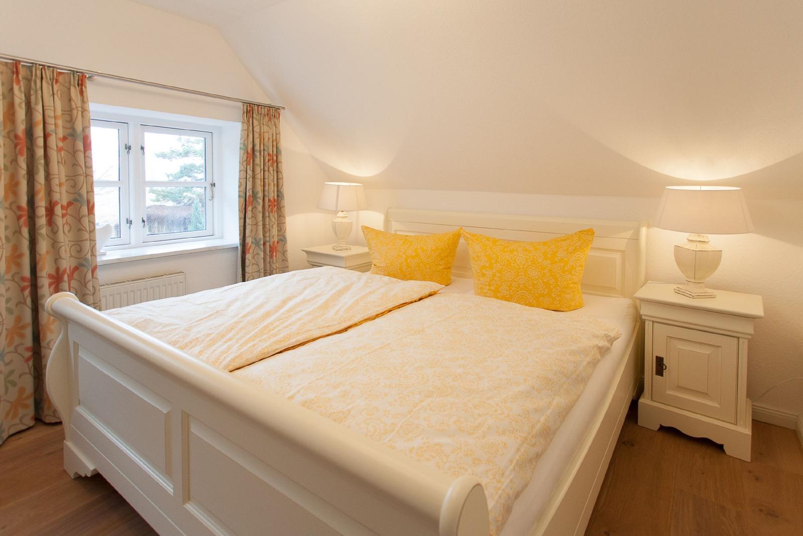 Schlafzimmer mit weißem Bett, gelben Kissen und Nachttischen mit Lampen.