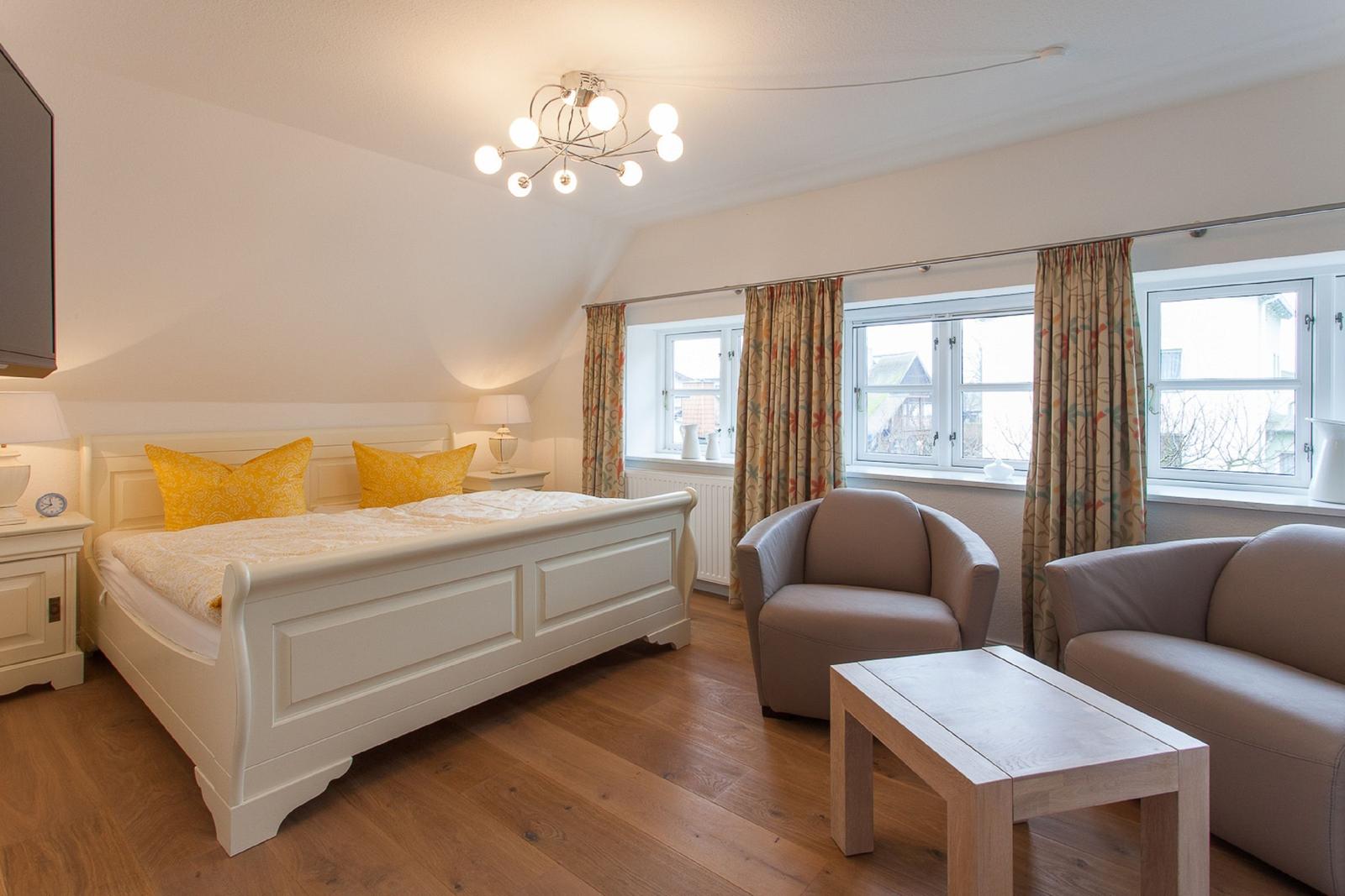 Schlafzimmer mit Bett, Sitzgelegenheiten und Fenstern mit Vorhängen.