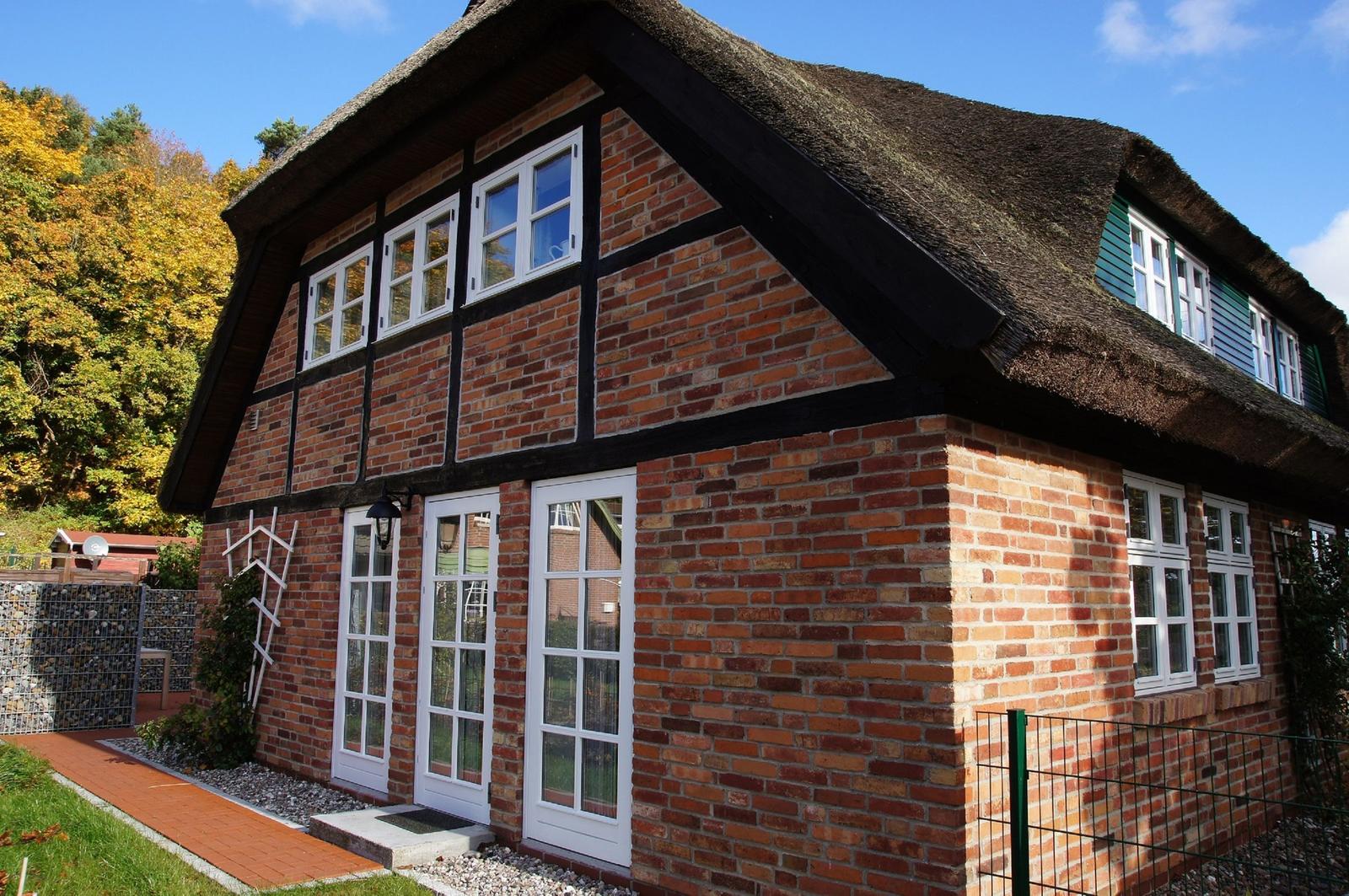 Rotes Backsteingebäude mit strohgedecktem Dach und weißen Fenstern.