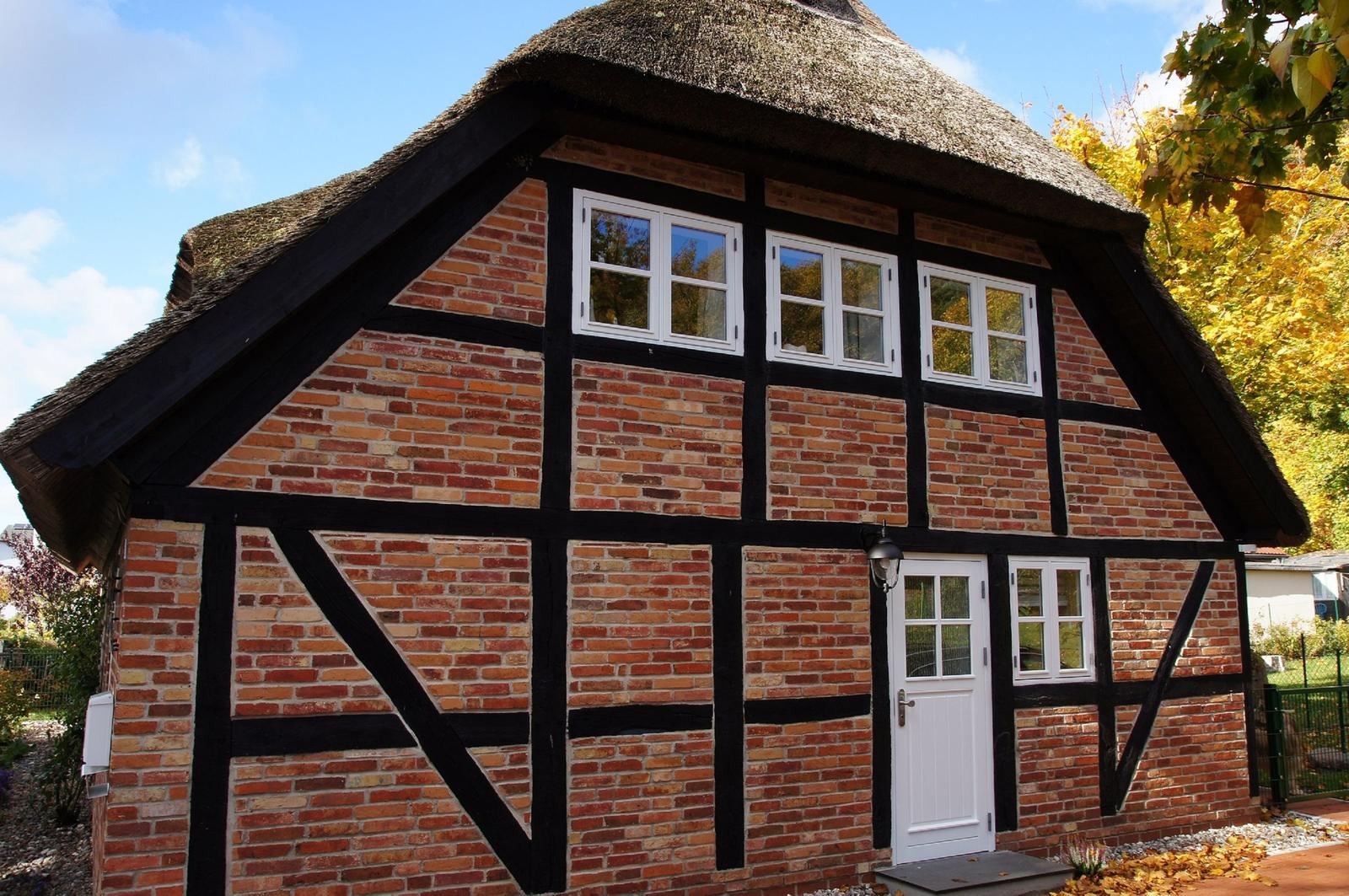 Haus mit strohgedecktem Dach, roten Ziegeln und weißen Fenstern.