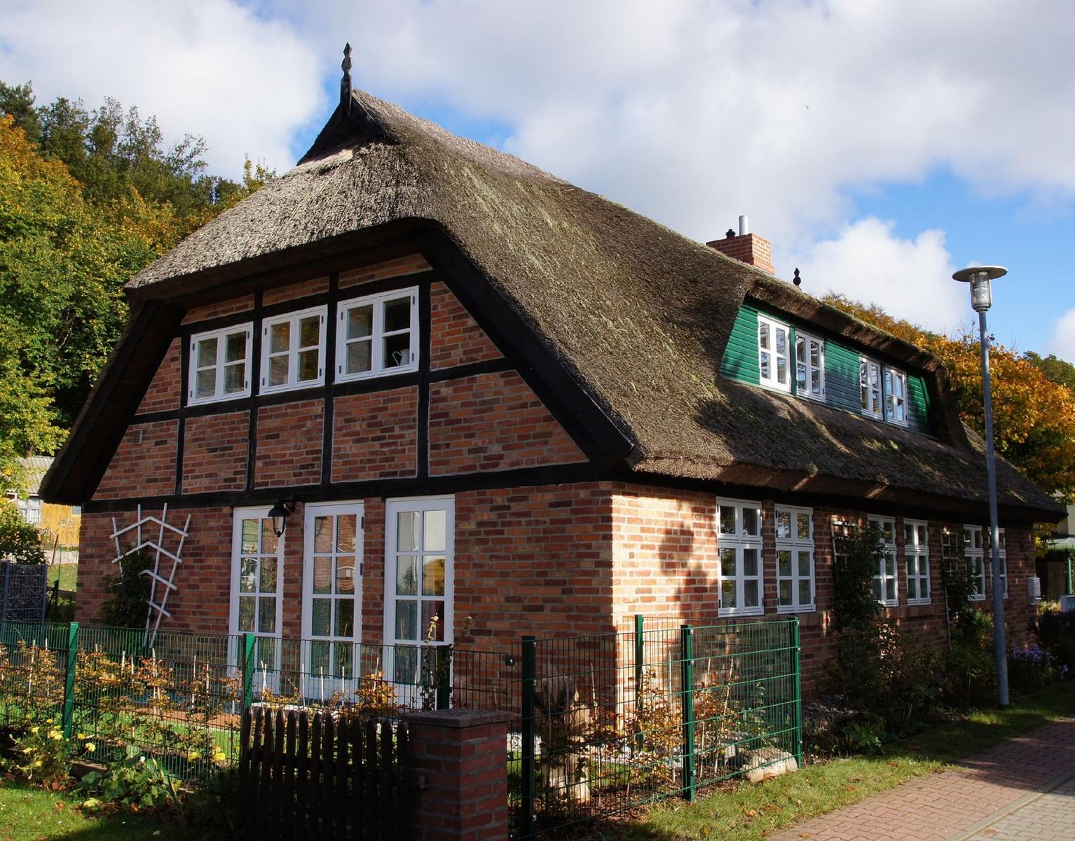 Rotes Backsteinhaus mit Strohdach und grünen Fensterläden.