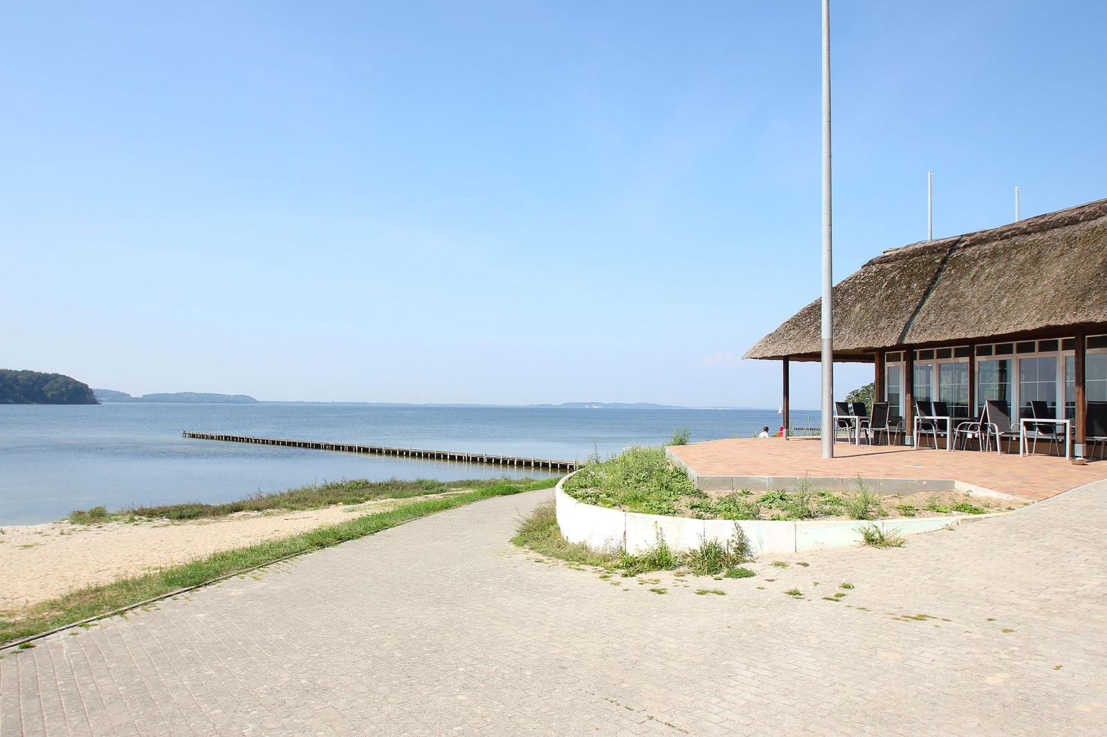 Haus mit Dach aus Stroh, Terrasse und Blick auf Wasser und Steg.