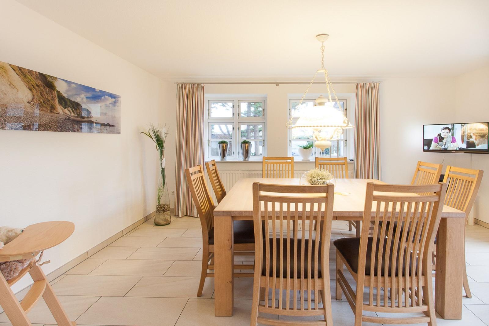 Esszimmer mit Holztisch, Stühlen und Fenstern. Wandbild und Deckenleuchte.