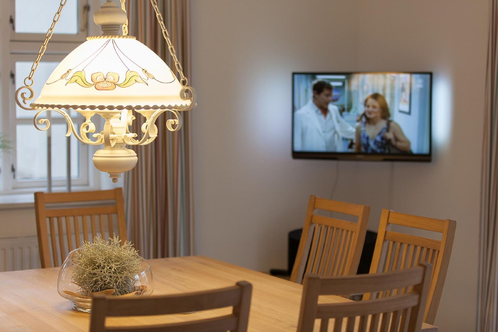 Esstisch mit Holzstühlen und Pendelleuchte. Fernseher an der Wand.