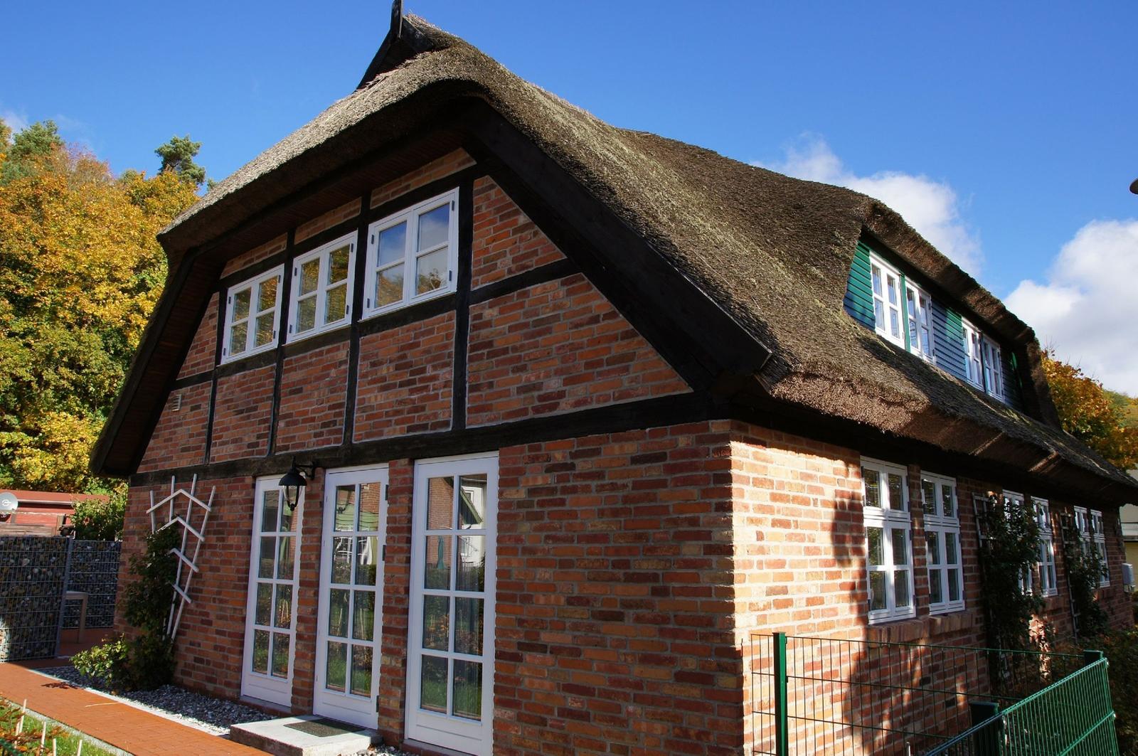 Haus mit strohgedecktem Dach, roten Ziegeln und weißen Fenstern.