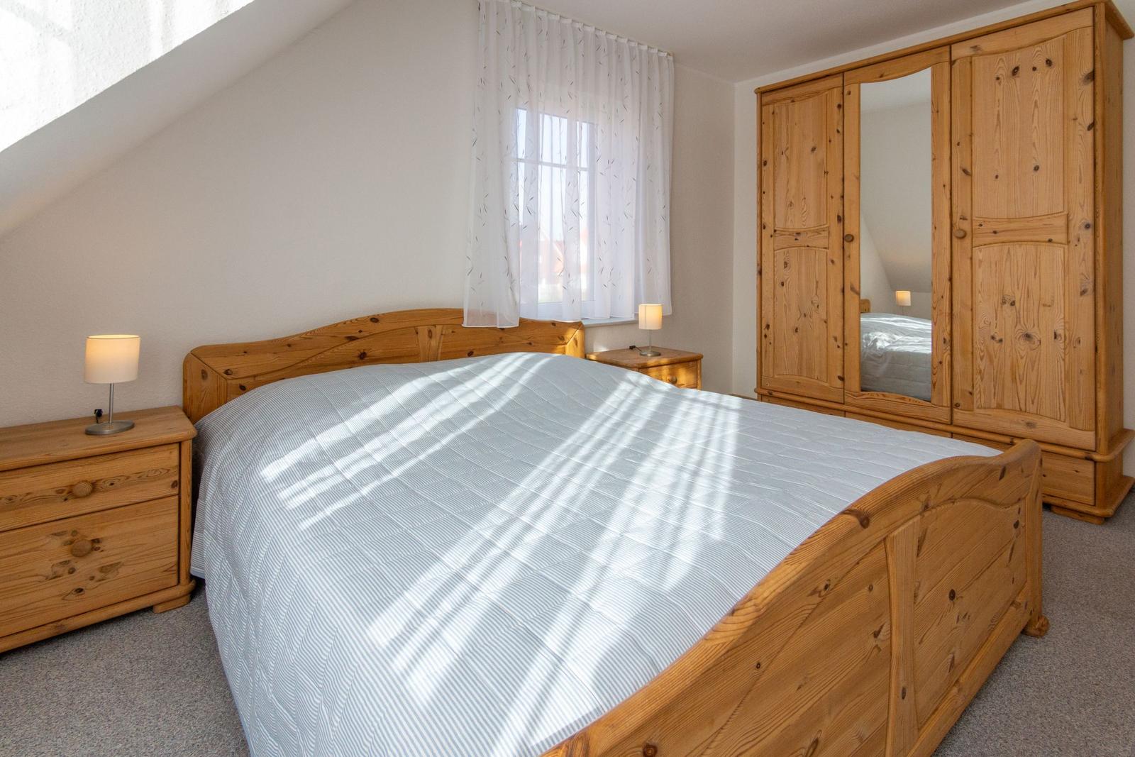 Schlafzimmer mit Holzbett, Schrank und Nachttischen unter Dachschrägen.