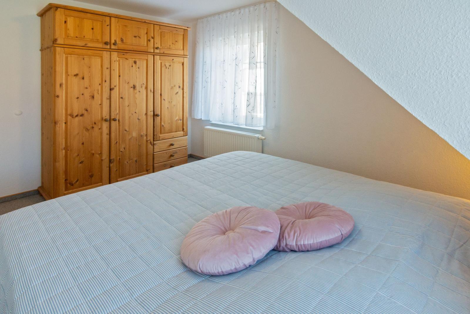 Schlafzimmer mit Holzschrank, Fenster und Bett mit Kissen.