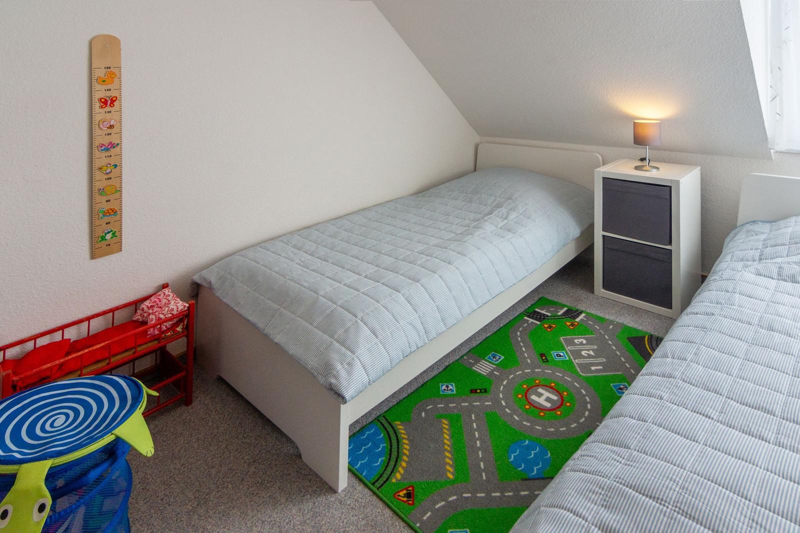 Zimmer mit zwei Betten, Spielteppich und Kinderhöhe-Messwand an der Wand.