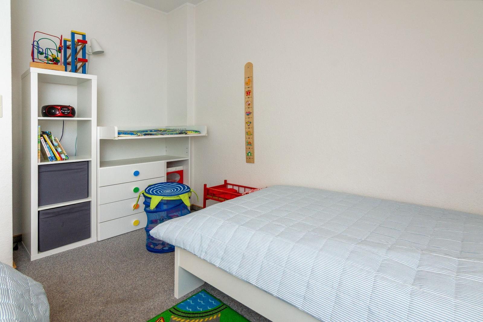 Kinderzimmer mit Bett, Regal, Spielzeug und Wachstumsmesser an der Wand.