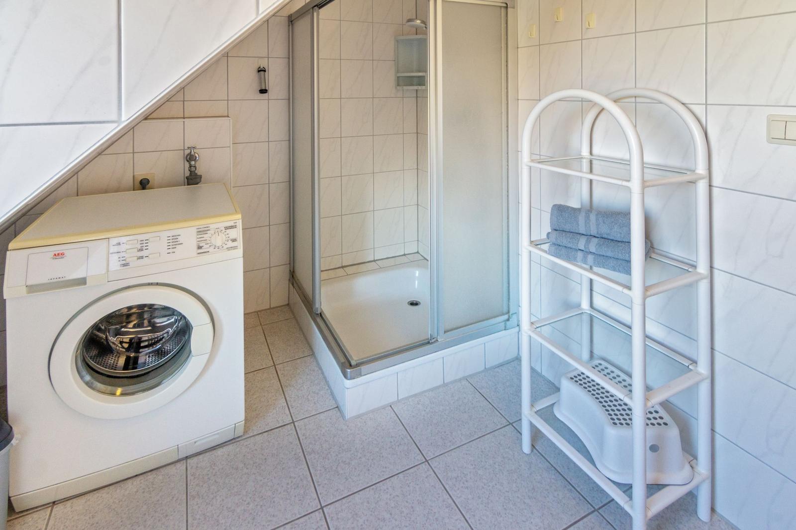 Badezimmer mit Dusche, Waschmaschine und Handtuchständer.