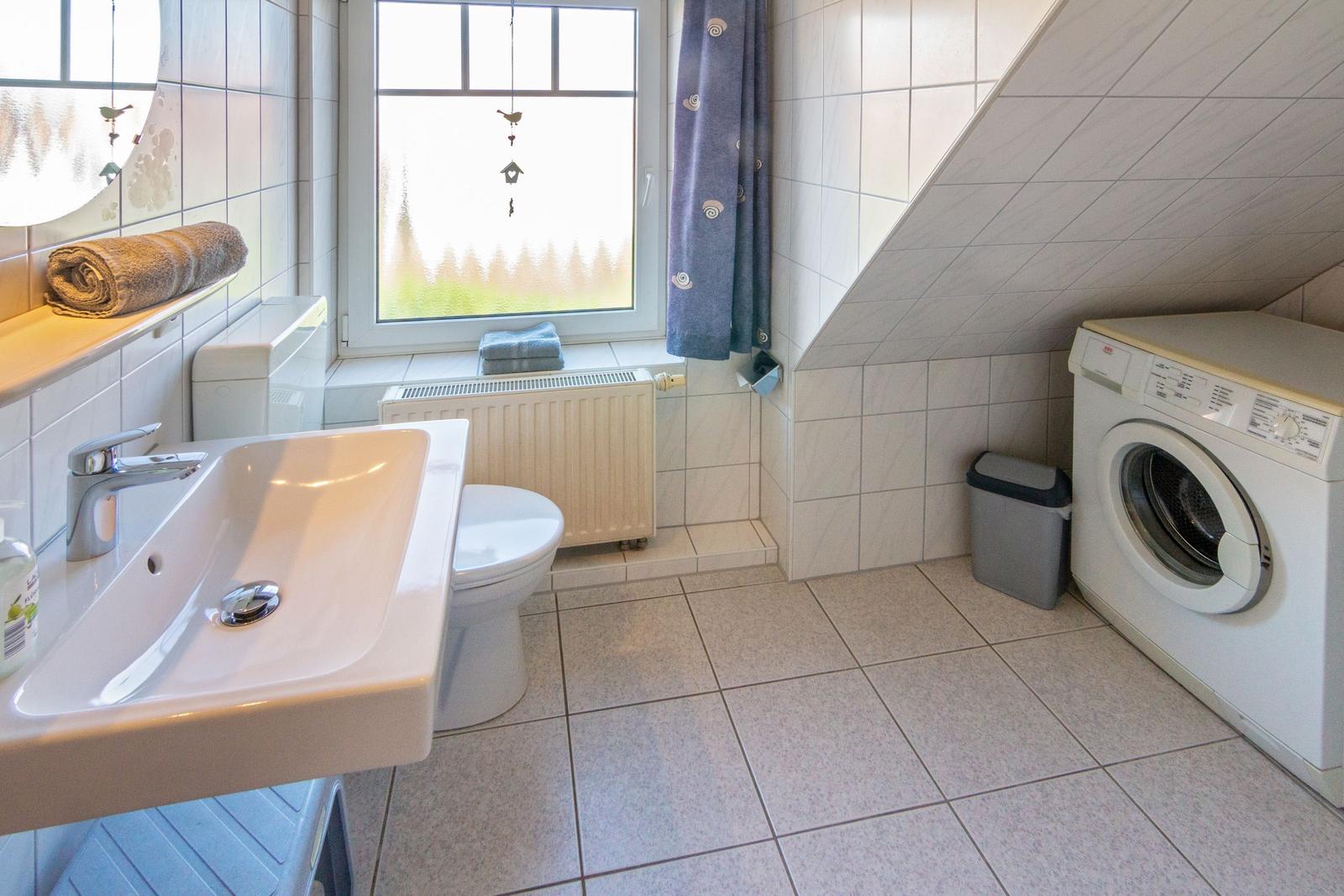Badezimmer mit Waschmaschine, Toilette und Waschbecken unter Dachschrägen.