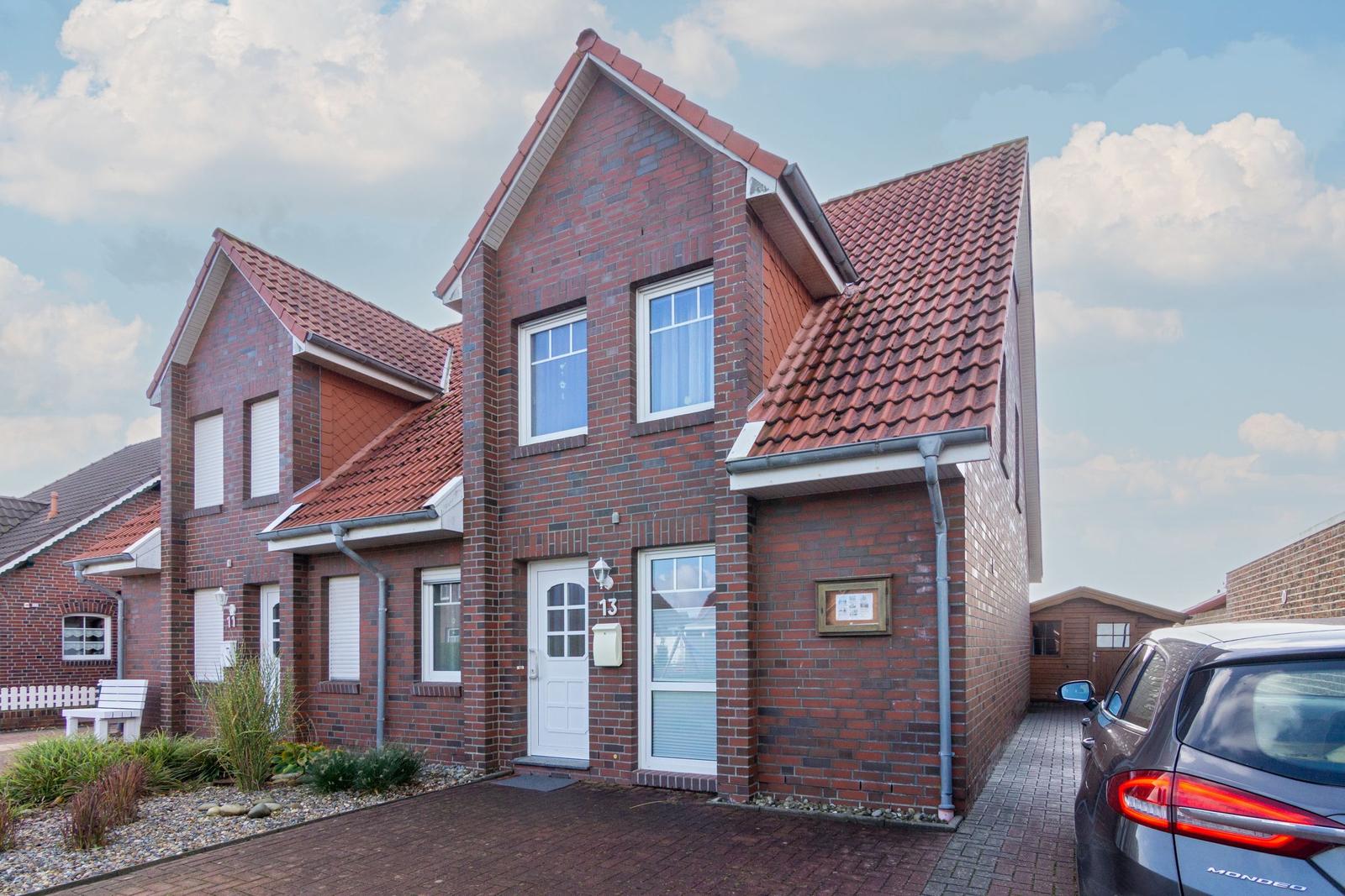 Rotes Ziegelhaus mit weißen Fenstern und Eingangstür. Vor dem Haus steht ein Auto.