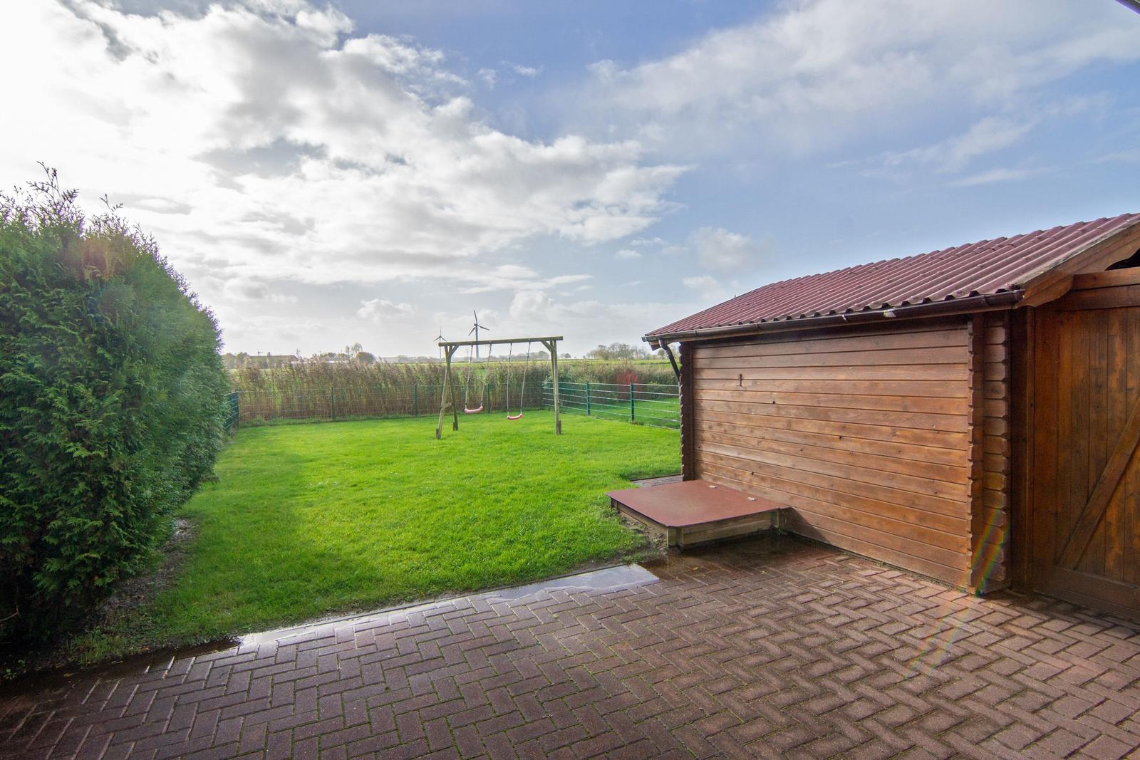 Hinterhof mit Spielgerüst, Rasen und Holzgarage unter bewölktem Himmel.