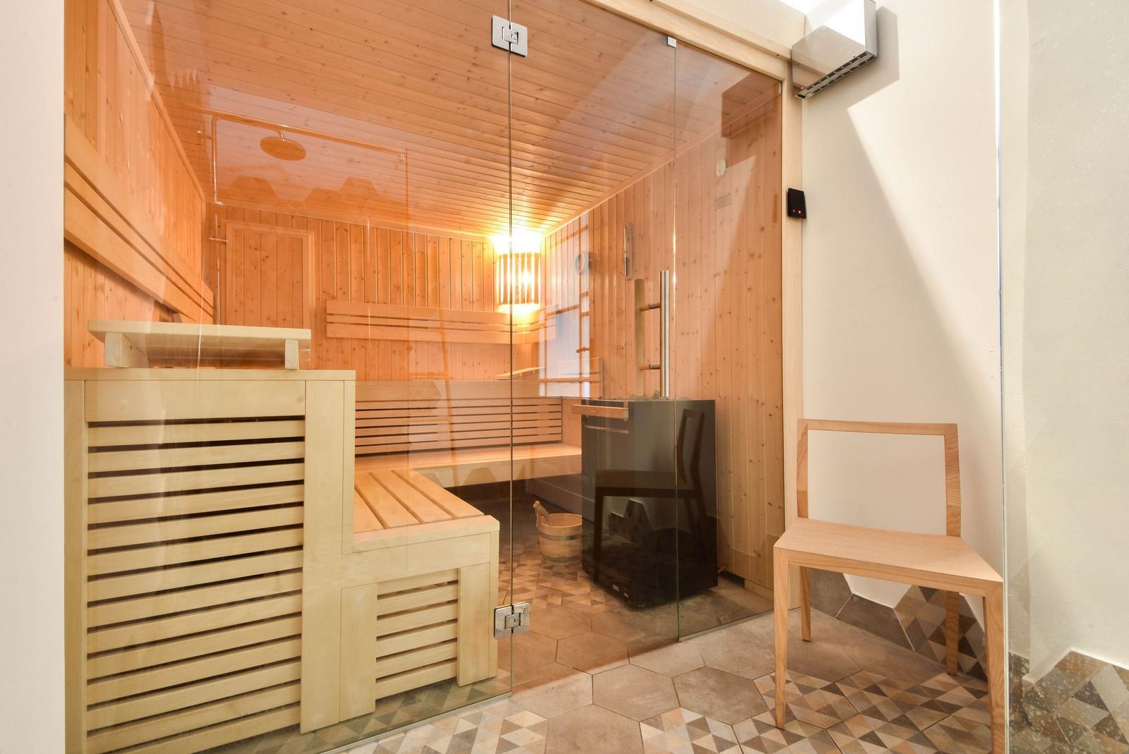Sauna mit Holzbank und Glaswand. Holzvertäfelung und Bodenfliesen.