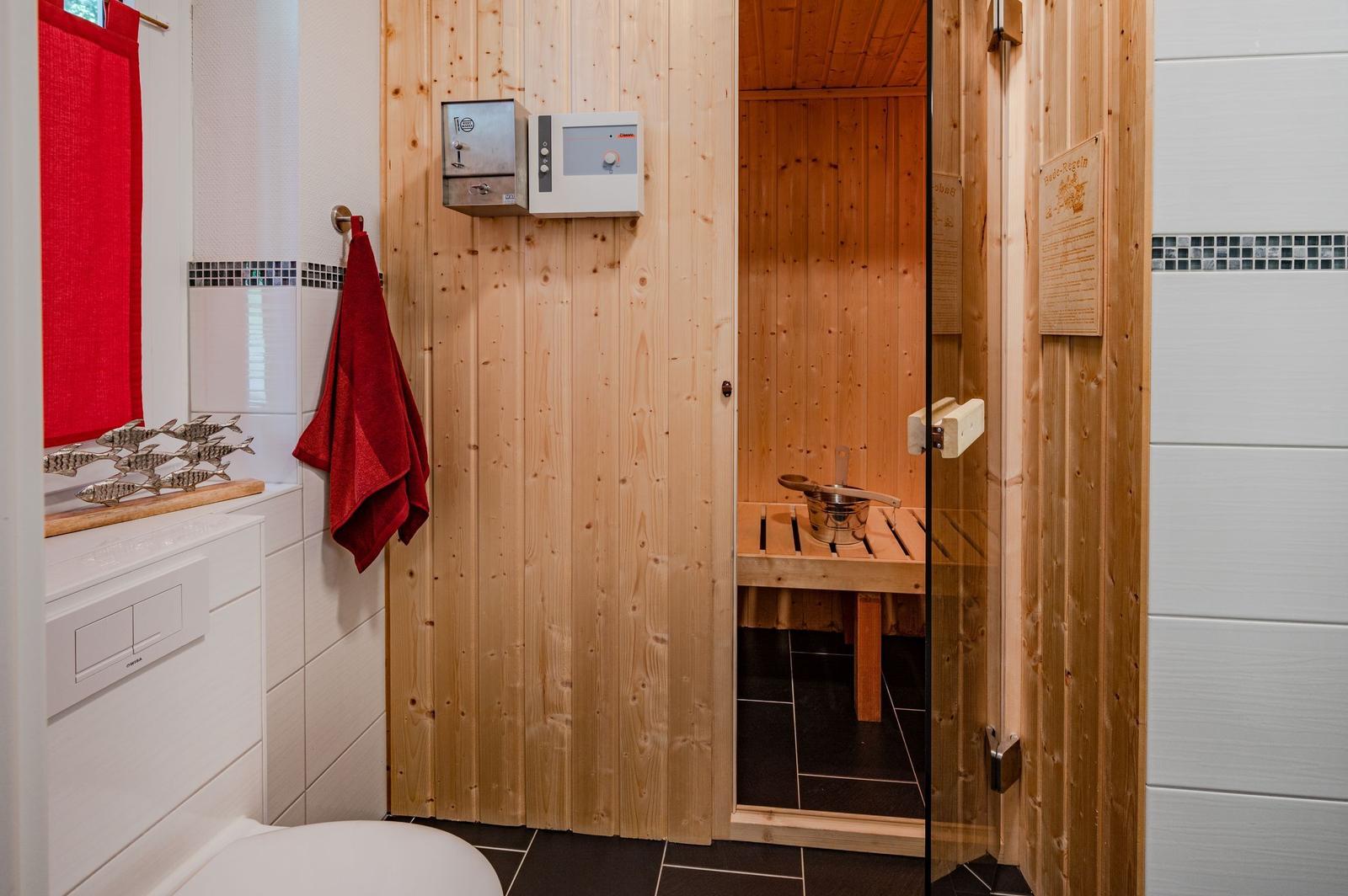 Sauna mit Holzwand und Sitzbank, daneben Badewanne mit rotem Handtuch.