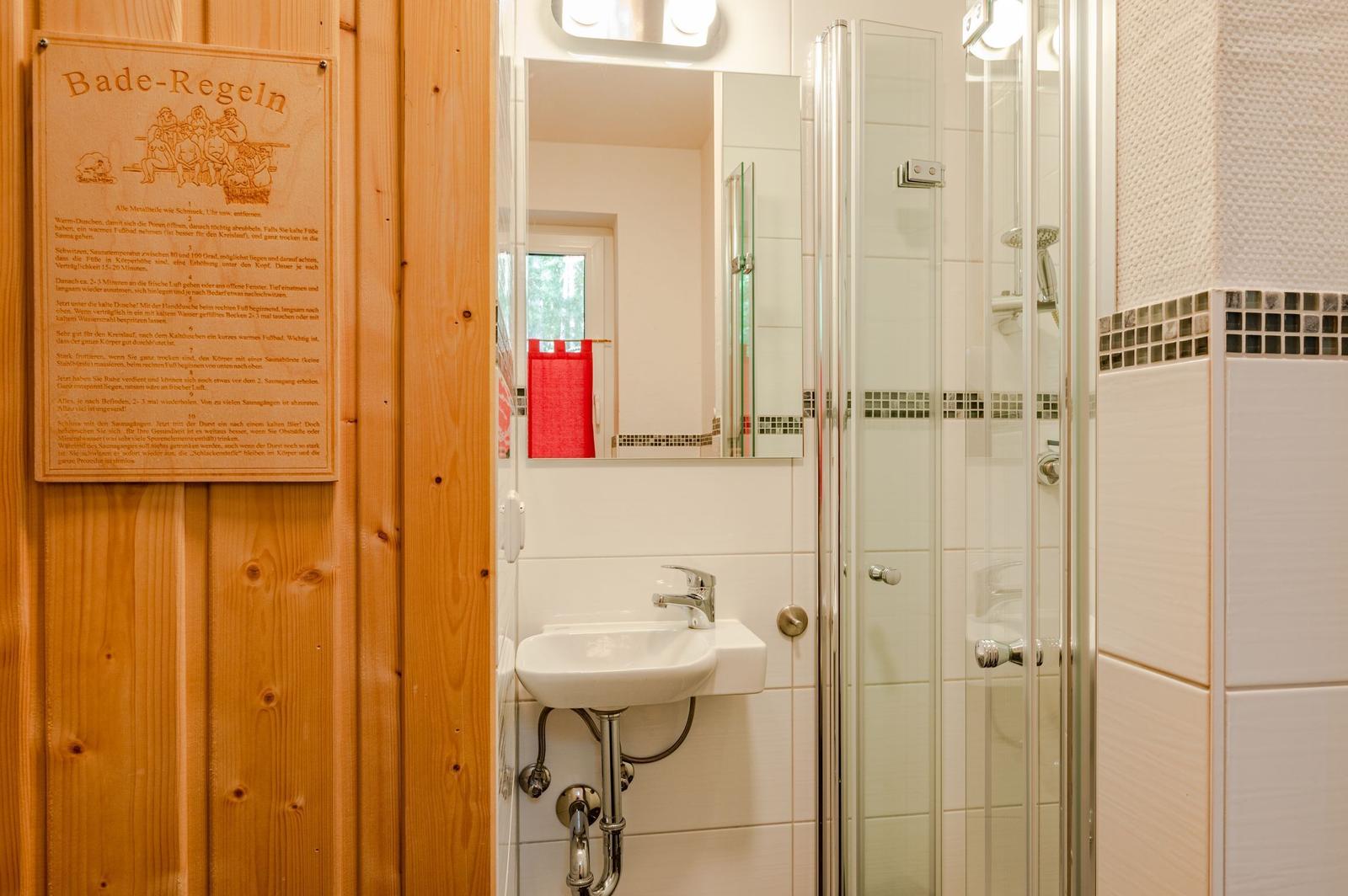 Badezimmer mit Dusche, Waschbecken und Baderegeln an Holzwand.