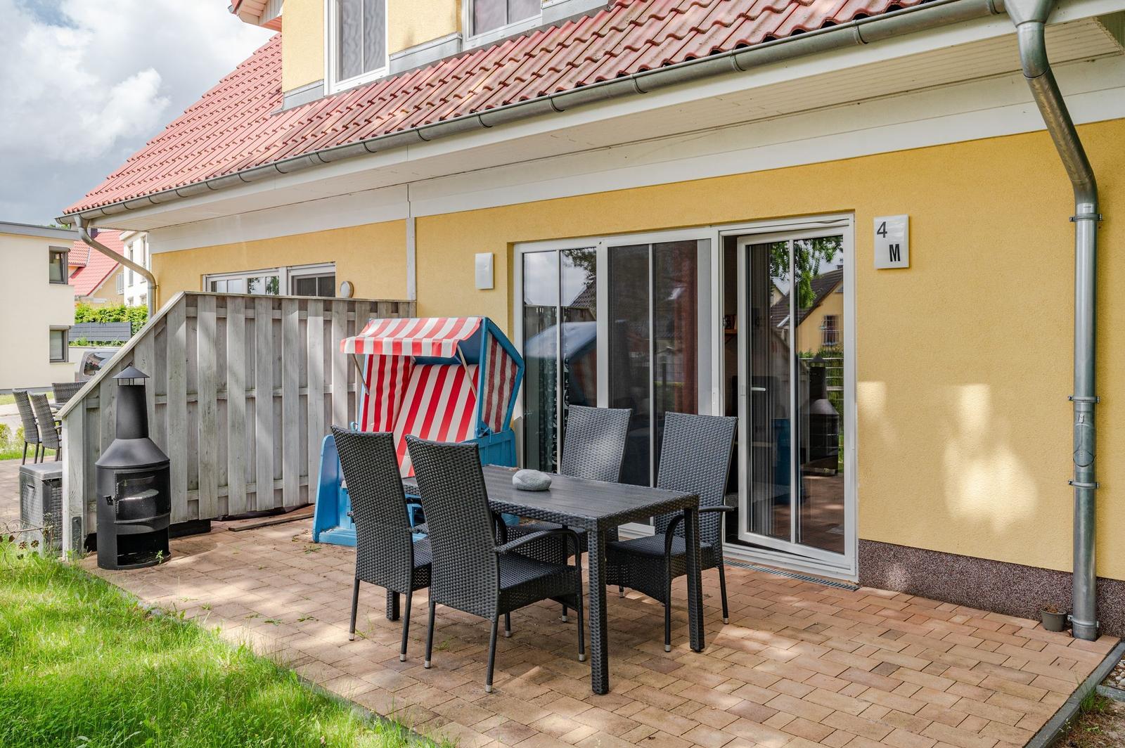 Terrasse mit Tisch, Stühlen und Strandkorb. Haustür mit Glasfront. Gelber Hauswänden.