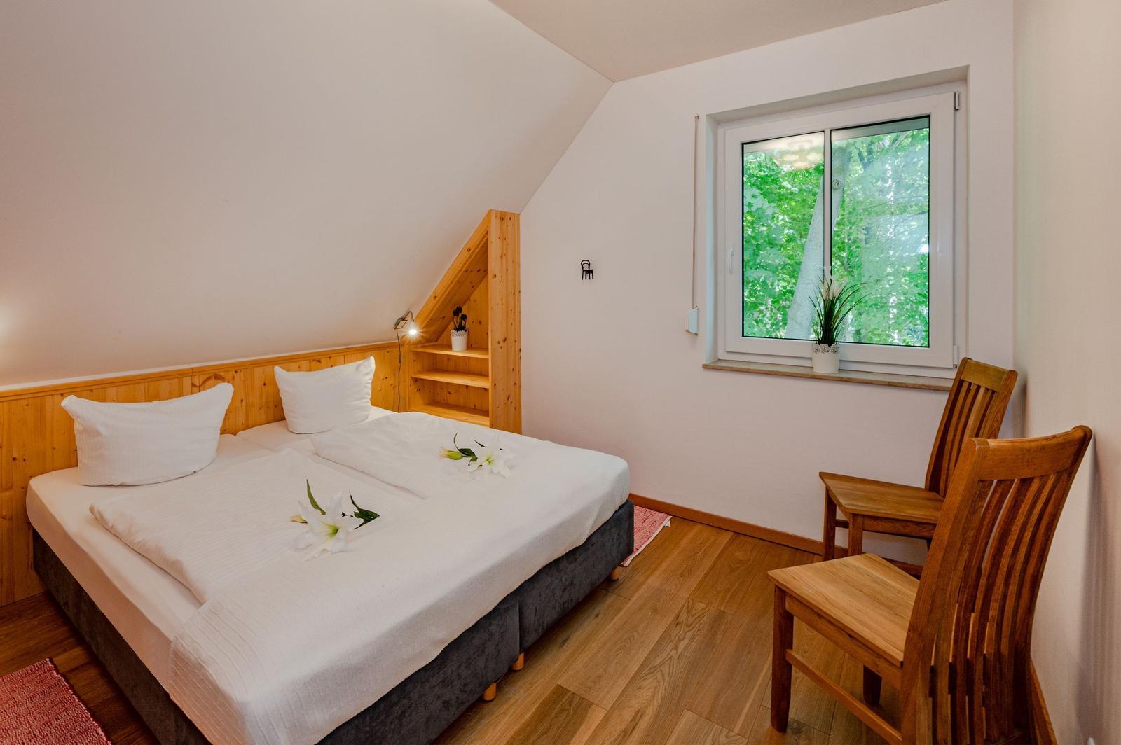 Schlafzimmer mit Doppelbett, Holzmöbel und Fenster mit Blick auf Bäume.
