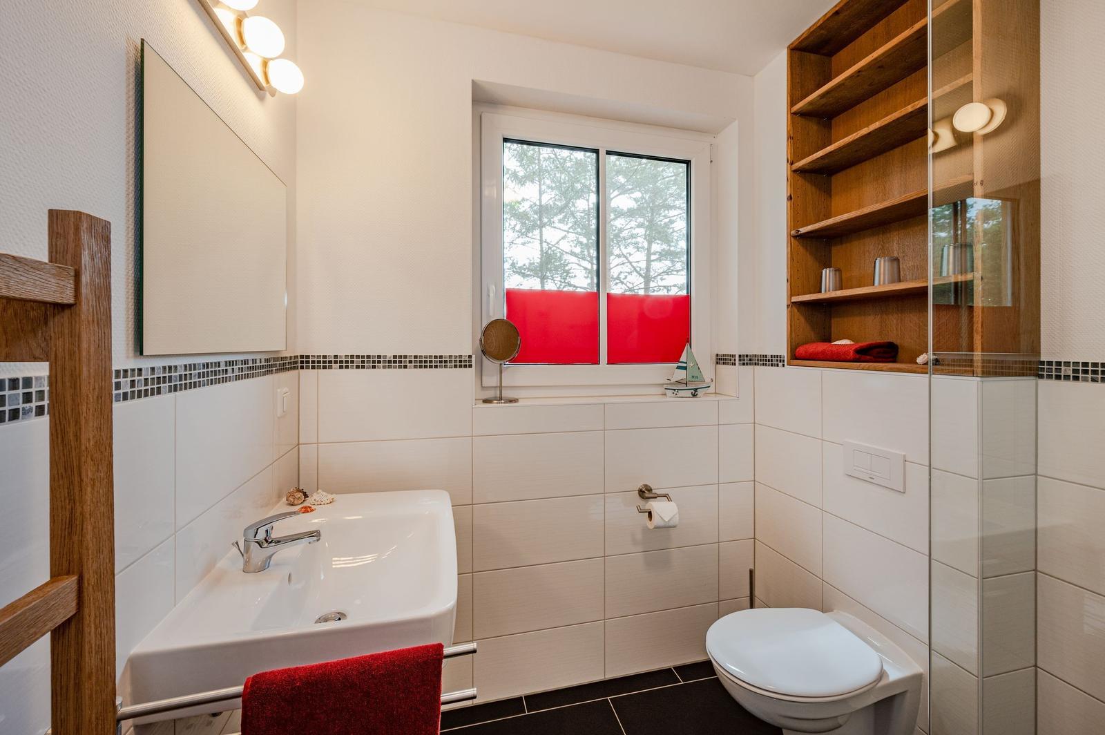 Badezimmer mit Waschbecken, Toilette und Fenster mit rotem Sichtschutz.