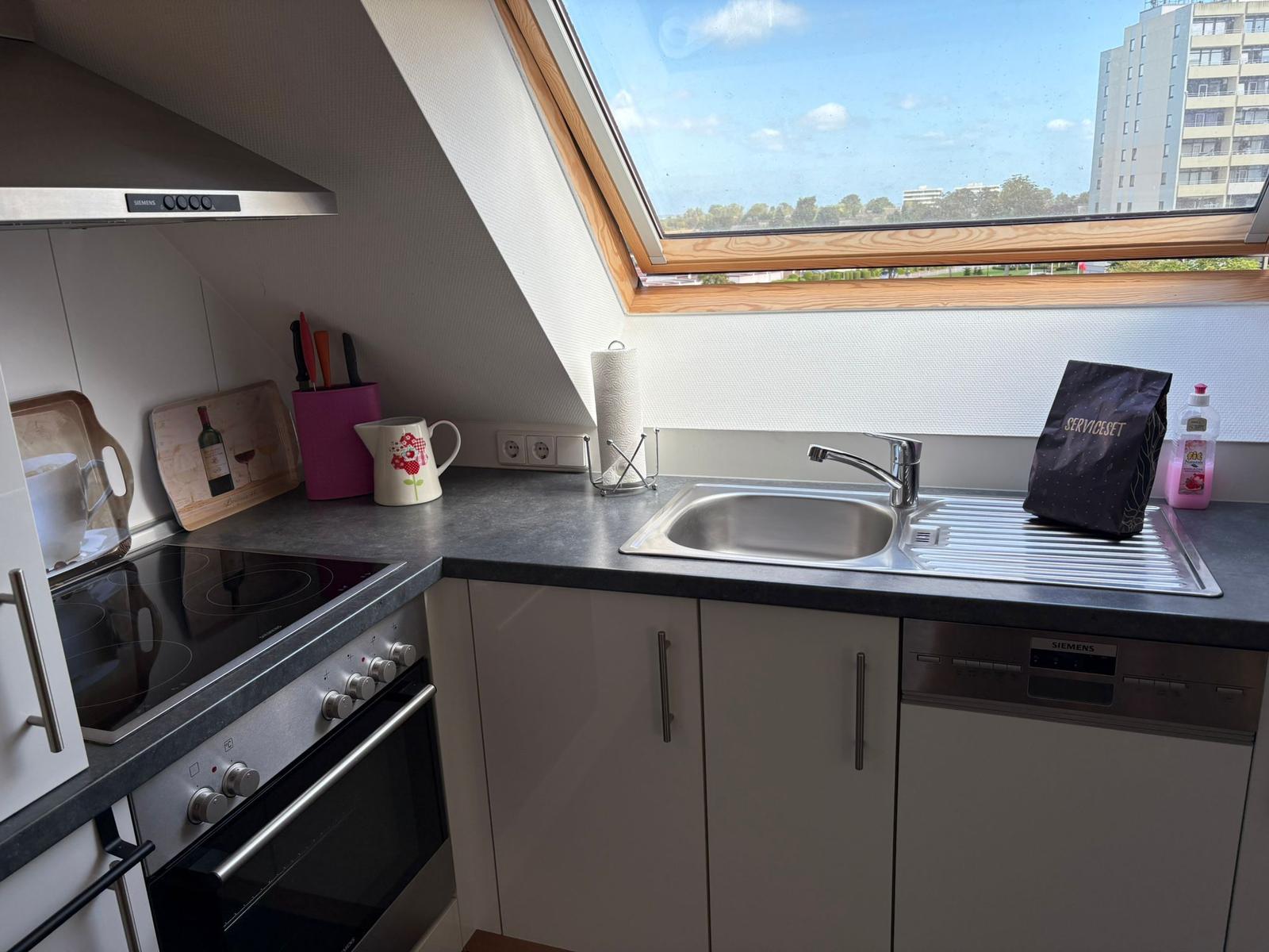 Küche mit Dunstabzugshaube, Spüle und Fenster. Geräte sind vorhanden.