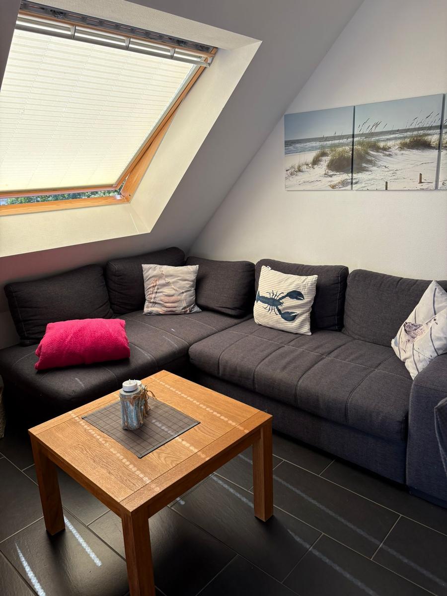 Ein Wohnbereich mit dunkelgrauem Sofa, Holztisch und Dachfenster.