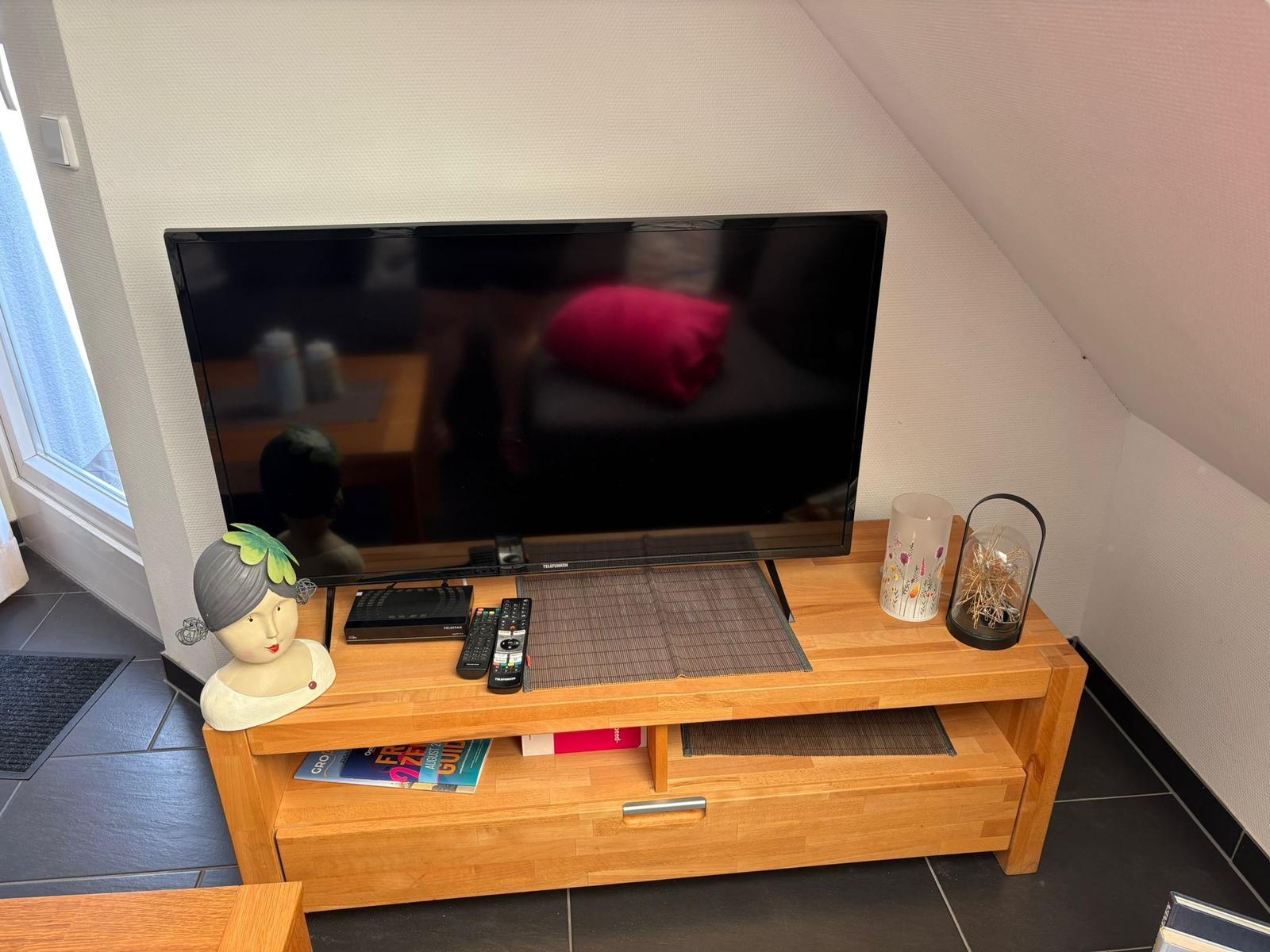 Flachbildfernseher auf Holz-TV-Schrank mit Dekoration und Fernbedienungen.