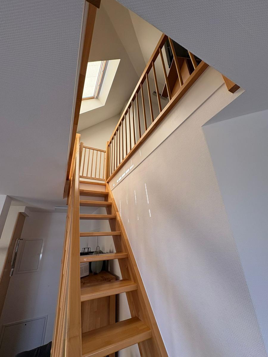 Holztreppe führt zur oberen Etage mit Dachfenster.