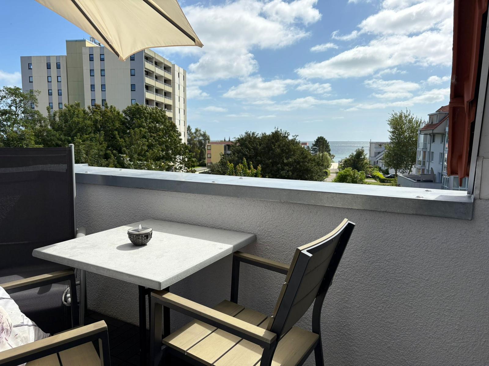 Terrasse mit Tisch und Stühlen, Blick auf Meer und Gebäude.