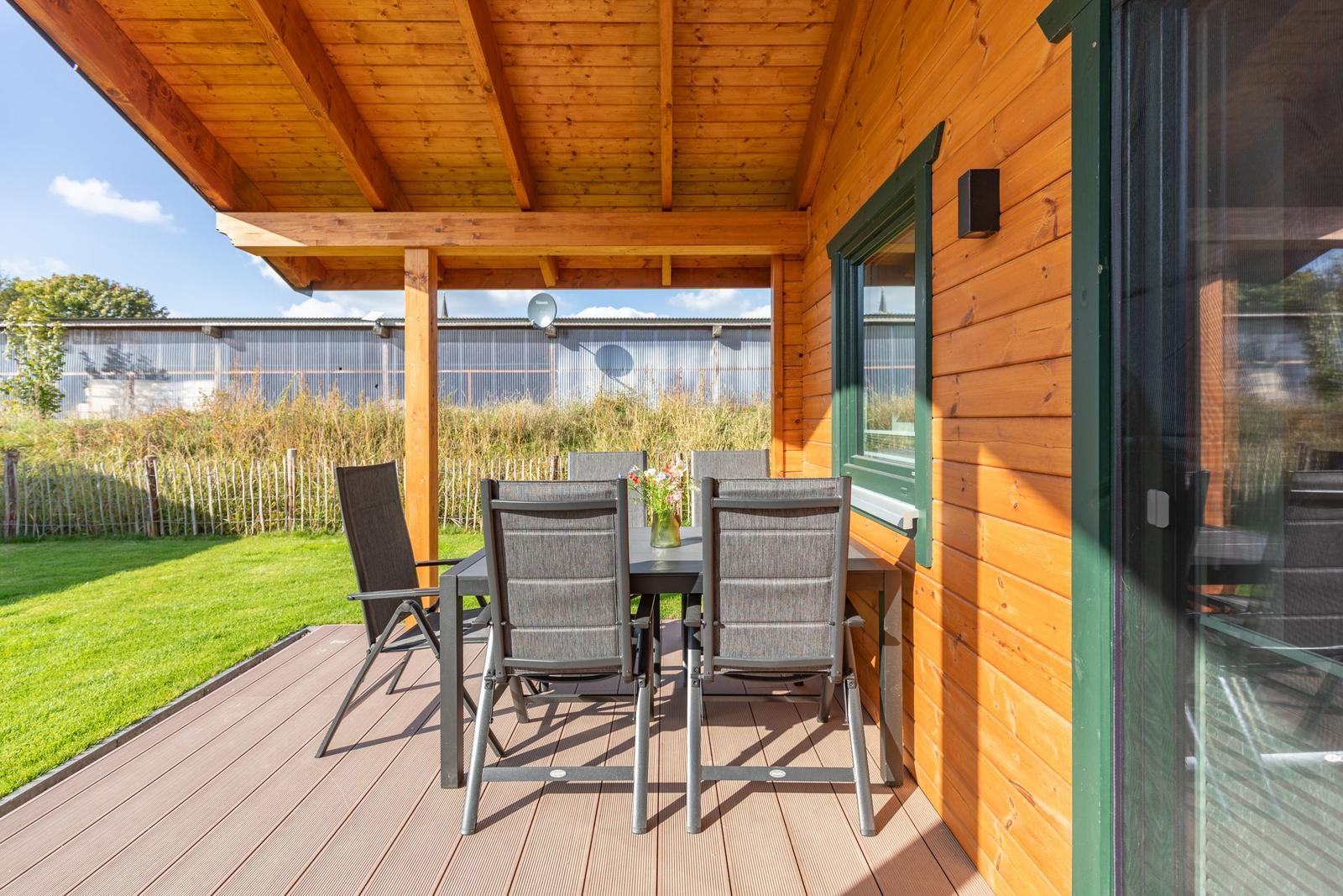 Terrasse mit Tisch und Stühlen neben Holzhäusern mit grünen Fensterrahmen.