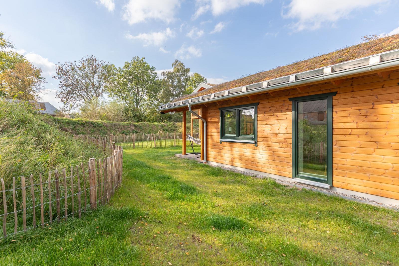 Holzhaus mit Grasdach, Garten und Hängematte unter freiem Himmel.