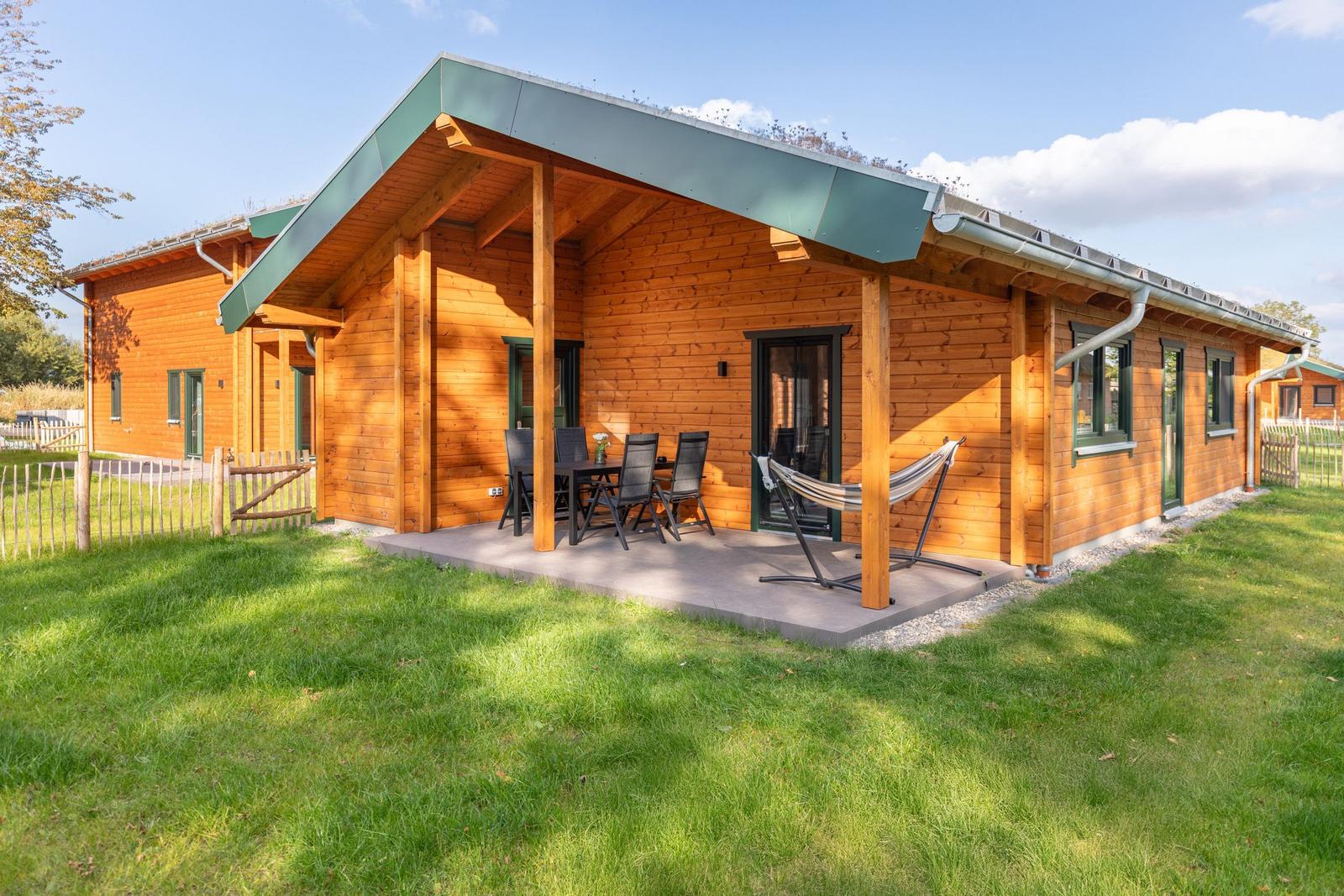 Holzhaus mit Terrasse, Tisch, Stühlen und Hängematte im Garten.