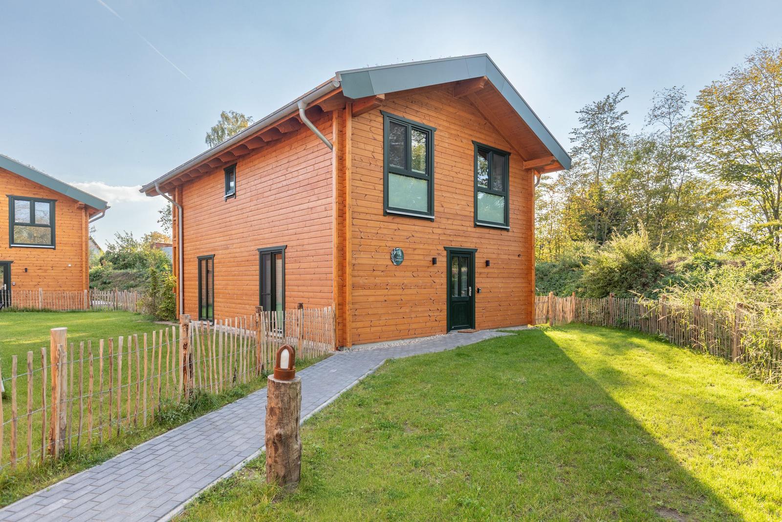 Holzhaus mit grünem Dach und Gartenweg. Umgeben von Gras und Bäumen.