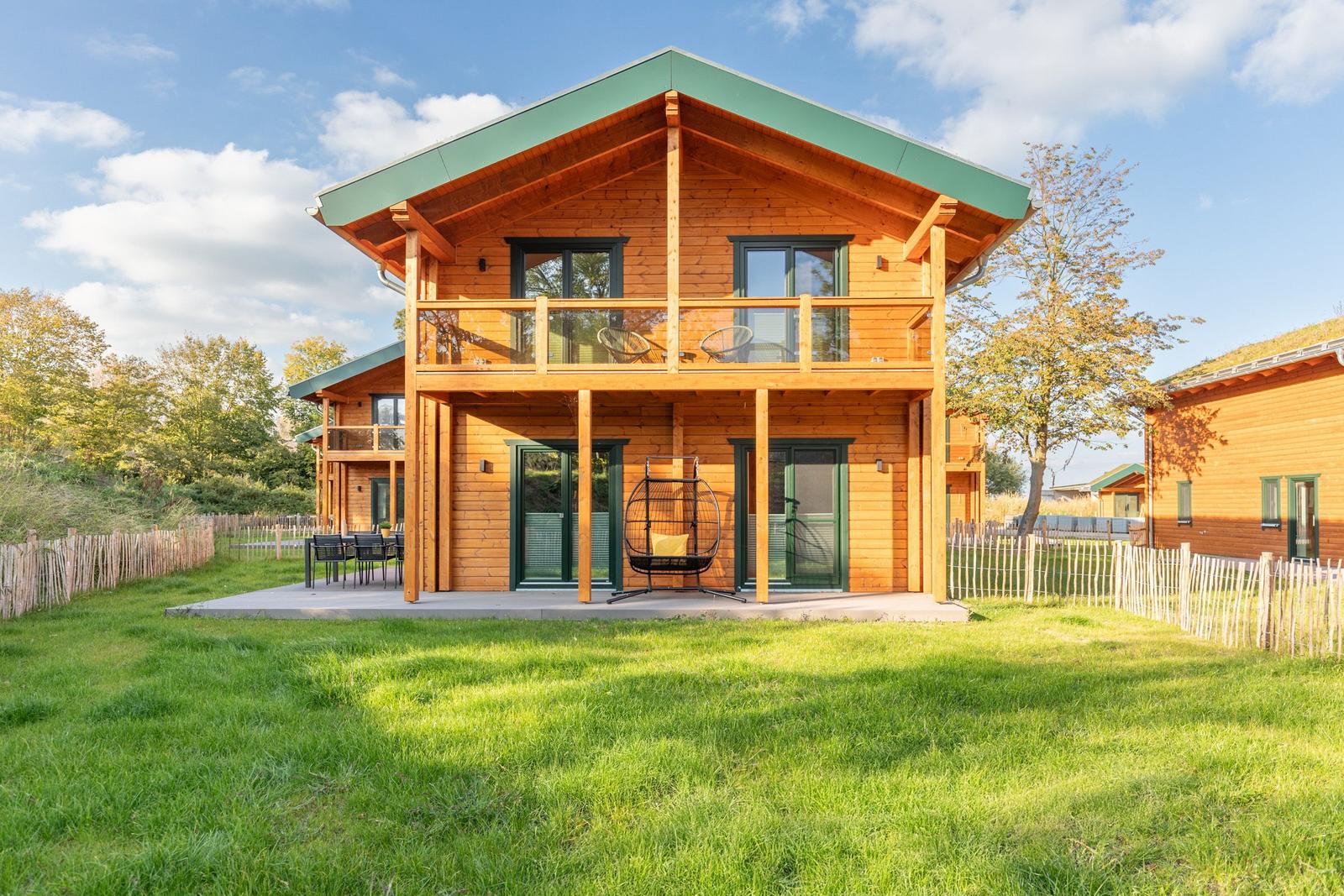 Holzhaus mit Balkon, Terrasse und Garten. Grüne Dachfläche und umliegende Bäume.