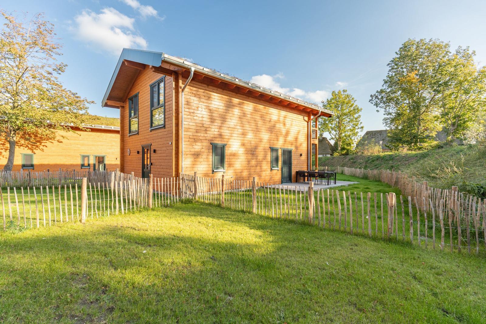 Holzhaus mit Garten und Terrasse. Umzäunt mit Holzpfostenzaun.
