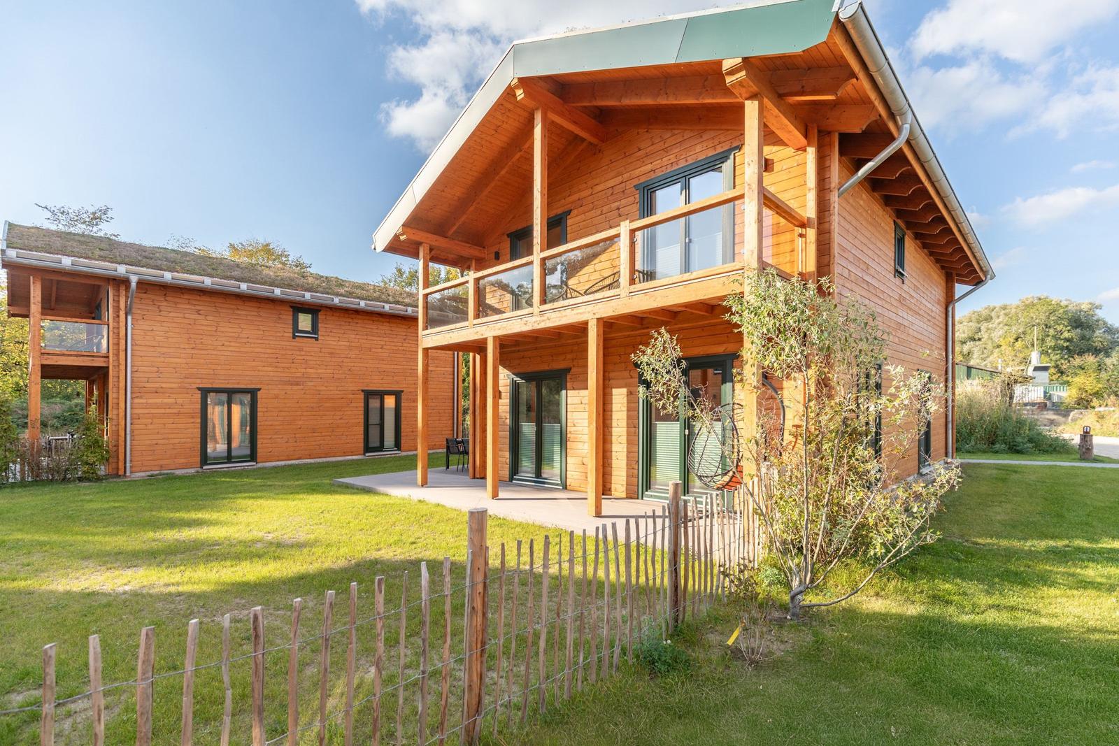 Holzhaus mit Balkon und Garten. Grünfläche und Zaun umgeben die Unterkunft.