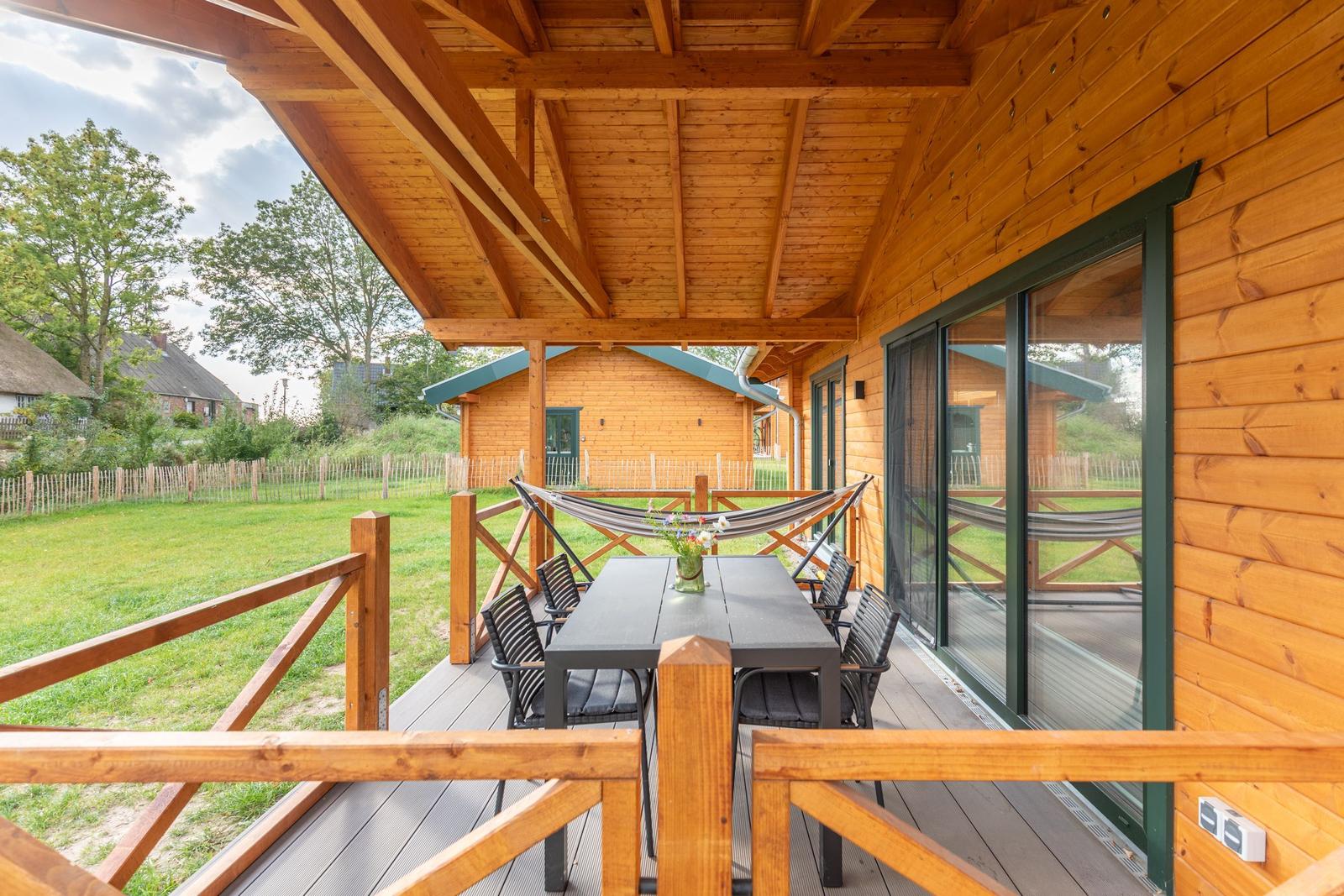 Terrasse mit Tisch, Stühlen und Hängematte. Holzveranda mit Blick auf Grünfläche.