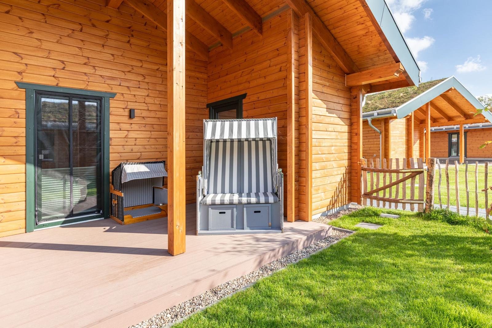 Holzterrasse mit Strandkörben und Gartenzaun. Hintergrund: weiteres Holzhaus.