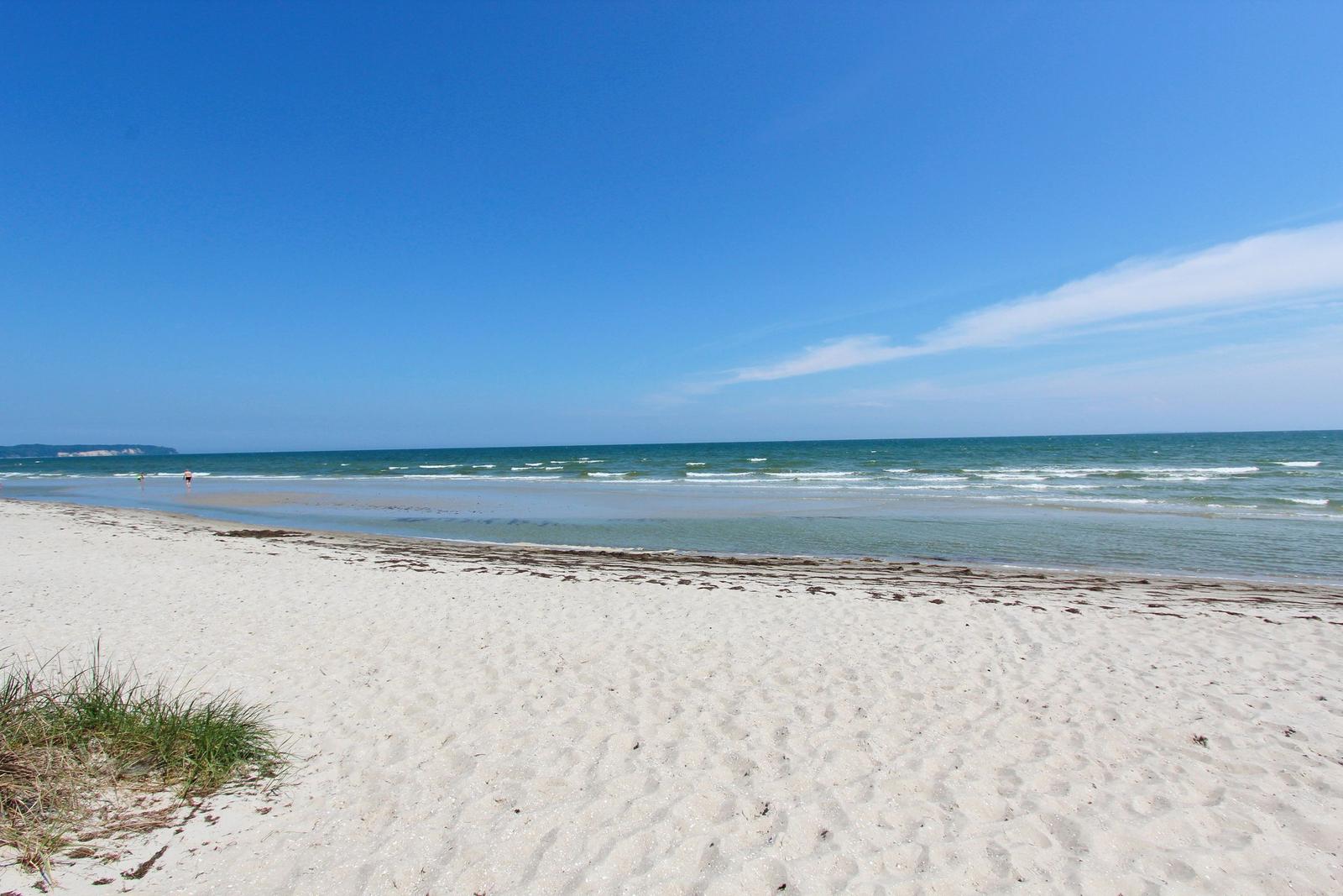 Weiterer Strand mit feinem Sand und tiefblauem Meer unter klarem Himmel.