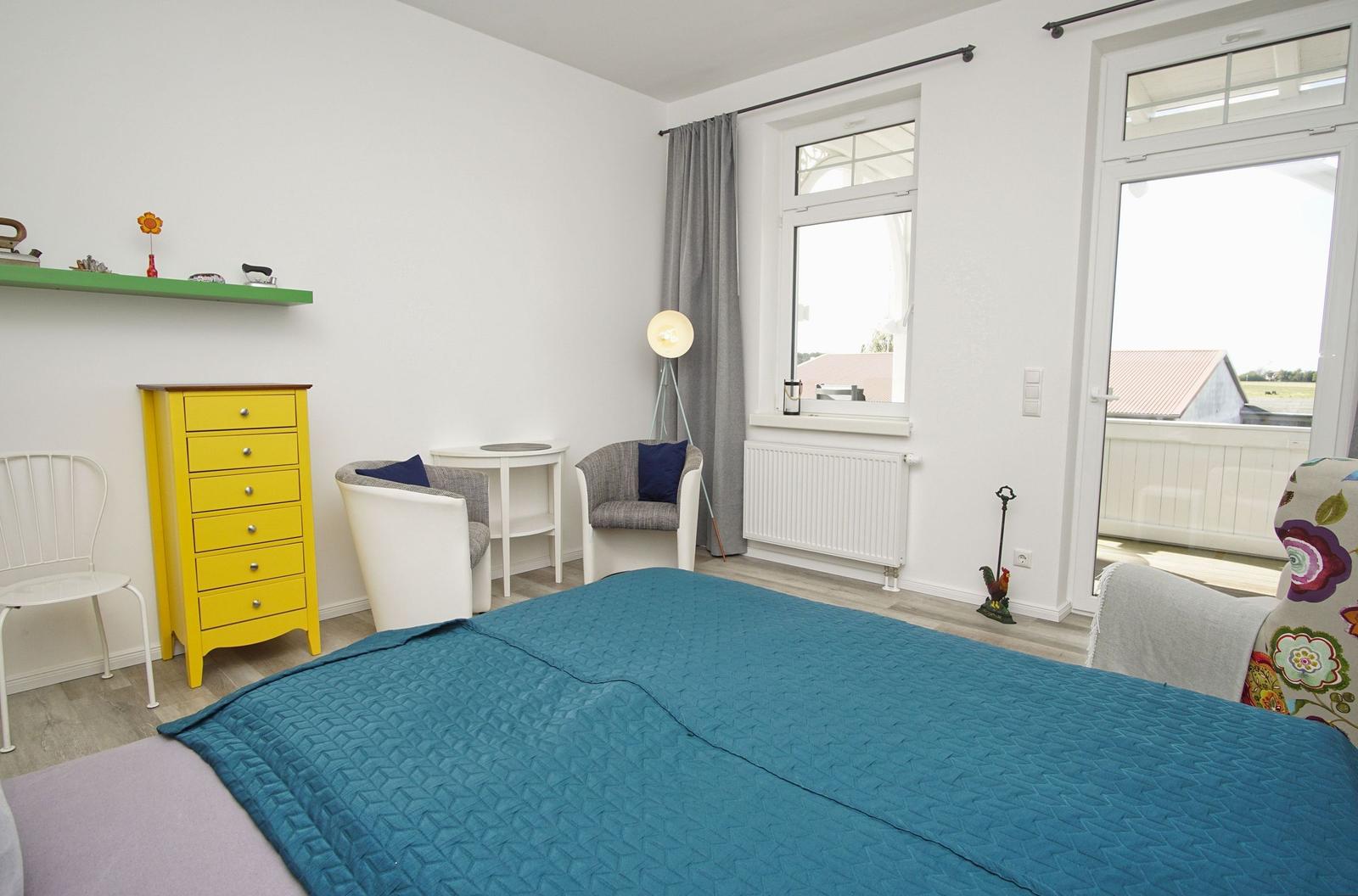 Schlafzimmer mit Bett, Schrank und Sitzgelegenheiten. Balkon mit Blick auf Felder.